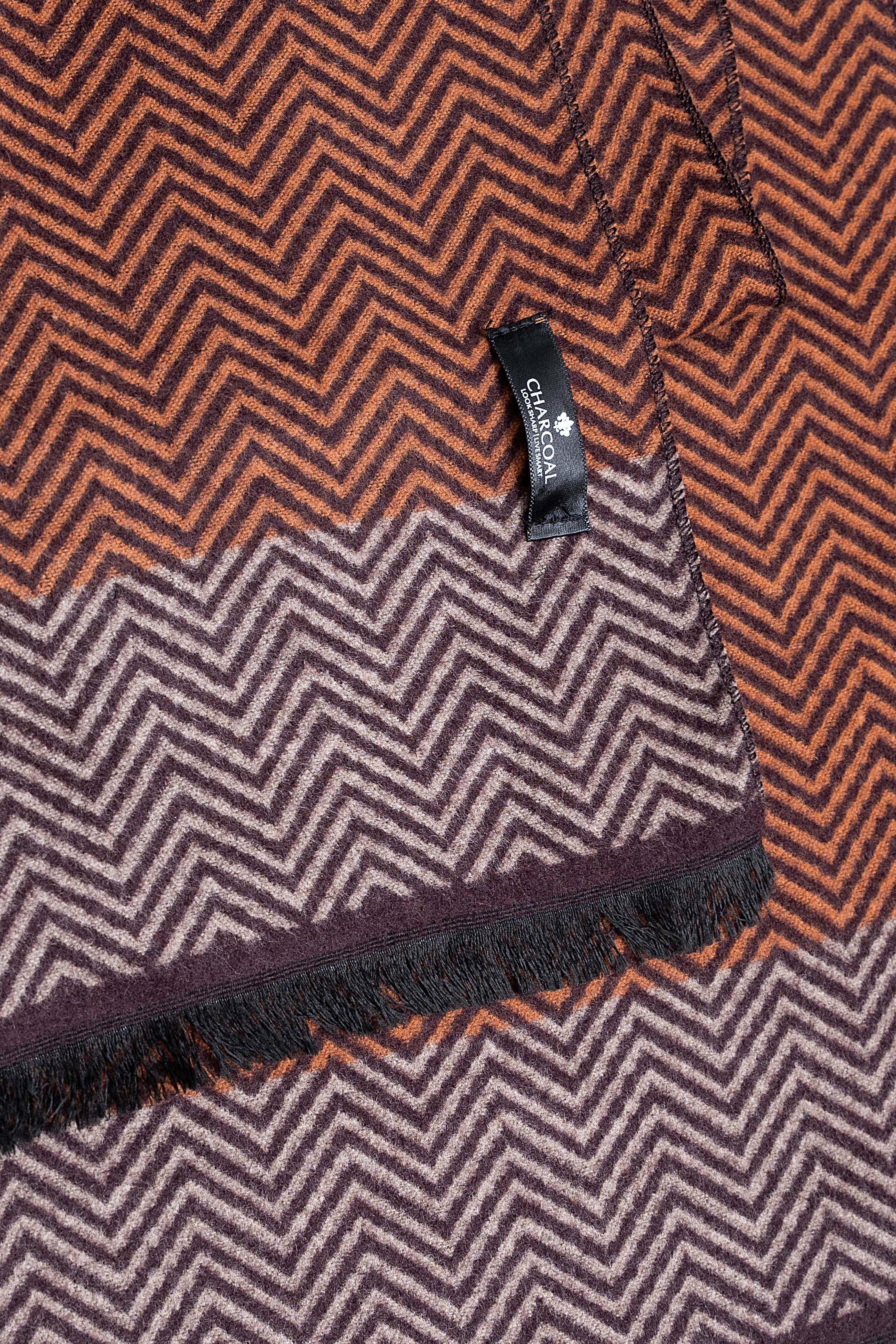 Chevron scarf close-up with brand label, rust brown zigzag weave and fringed border