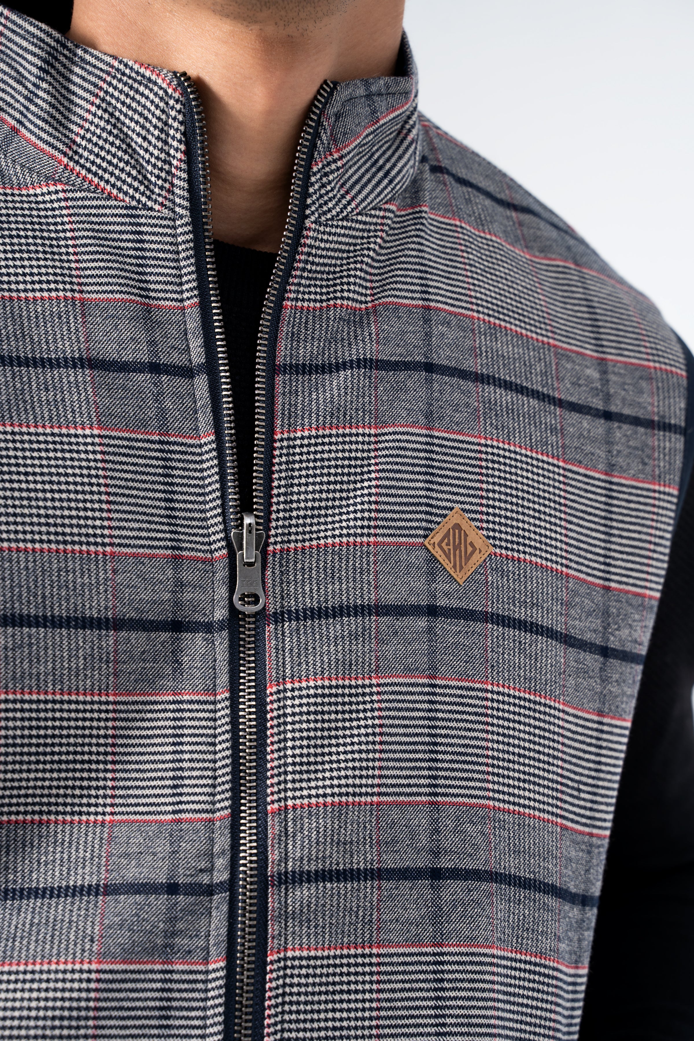 Quilted jacket panel in plaid gray with red stripes, visible zipper and logo patch