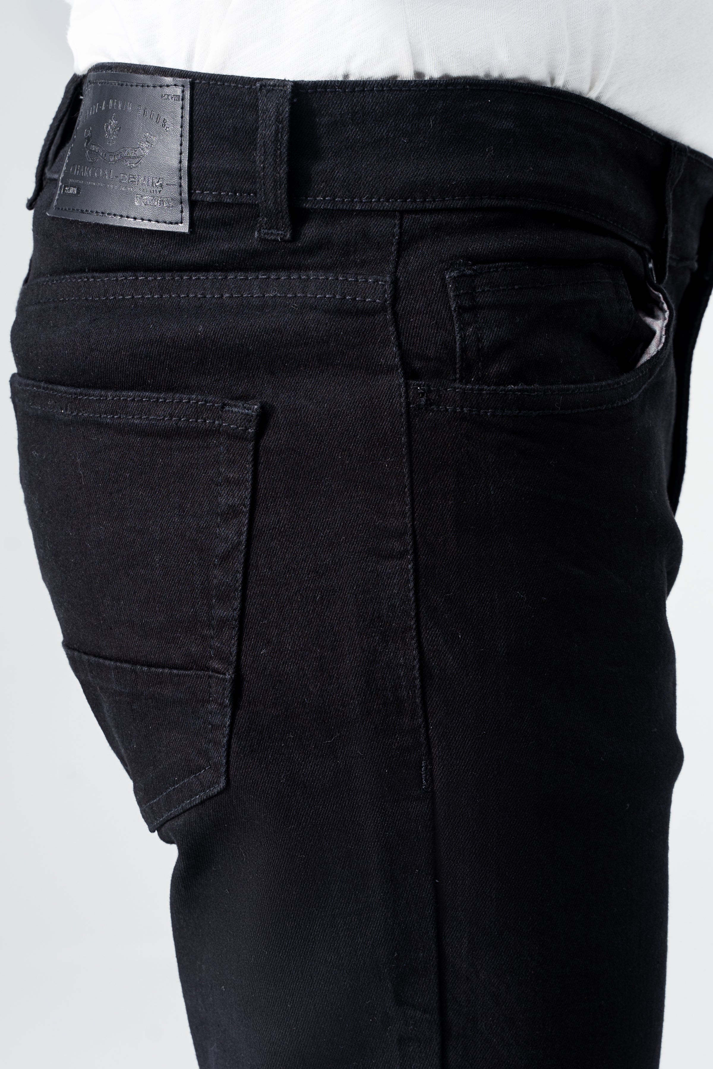 Black denim jeans close-up of waistband, belt loop, and label patch at fly