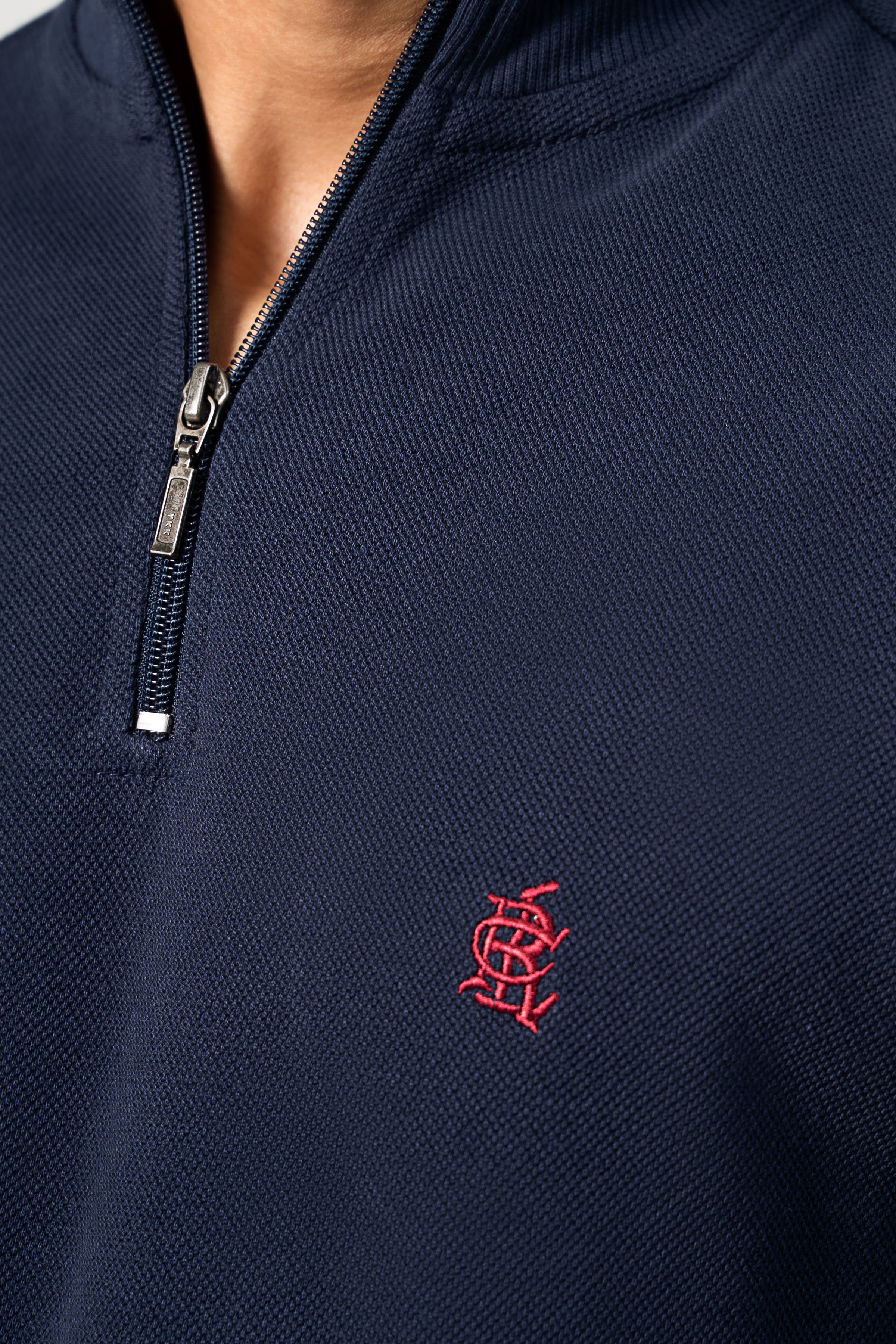 Navy mock-neck sweatshirt closeup: quarter-zip and red crest logo on chest