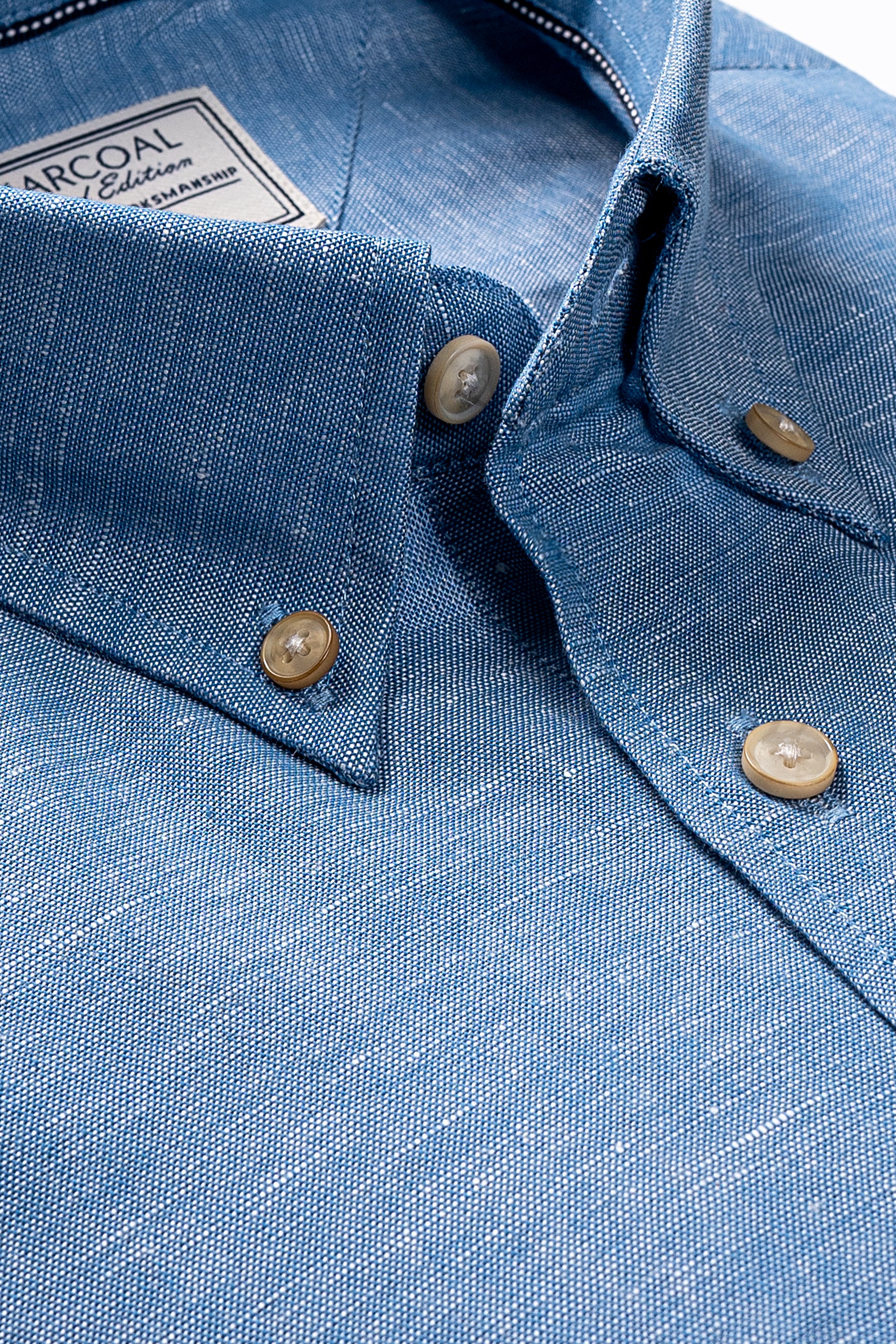 Blue chambray shirt close-up with pointed collar, tan buttons, and button placket