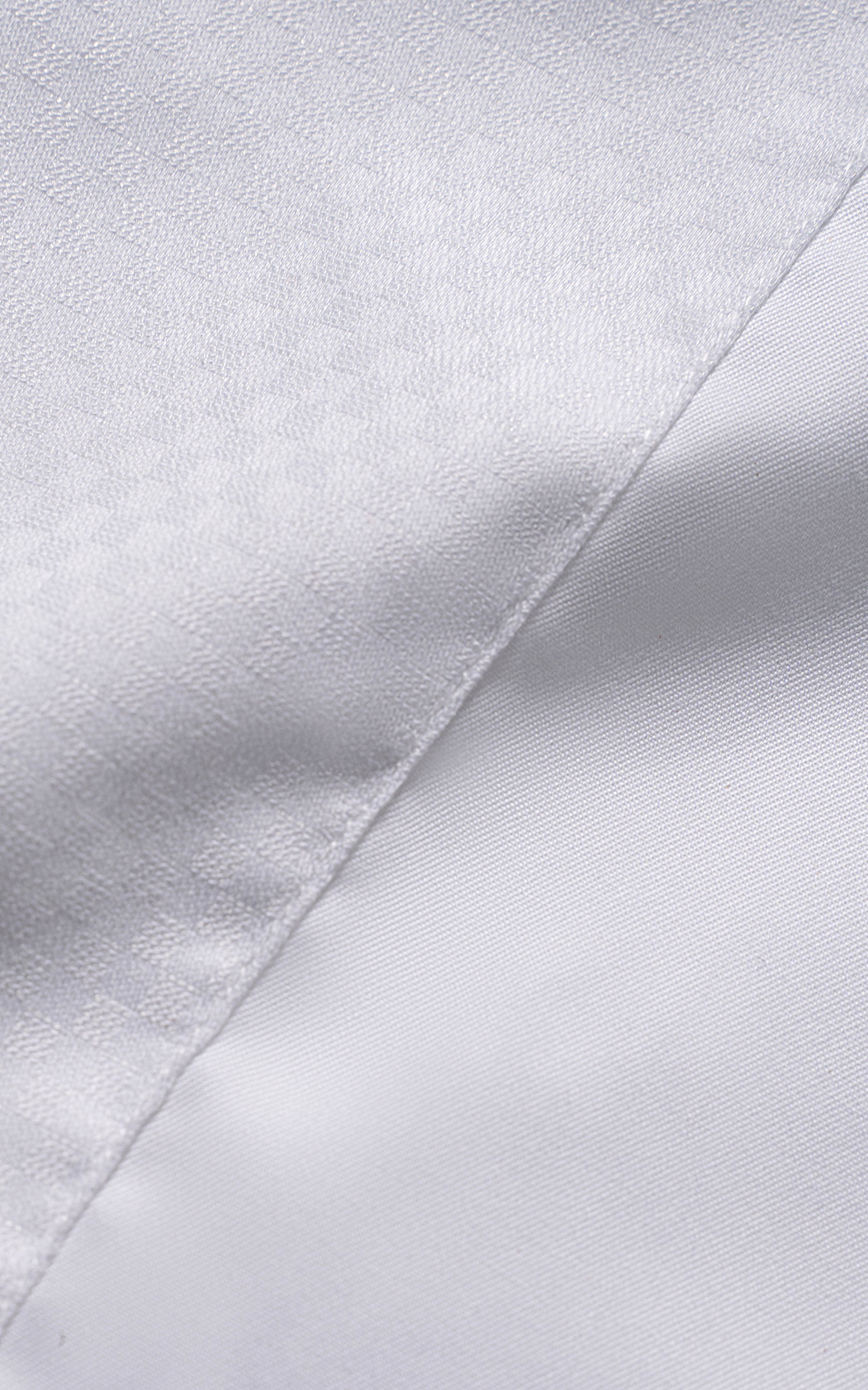 White dress shirt fabric close-up with subtle diagonal weave and stitched seam