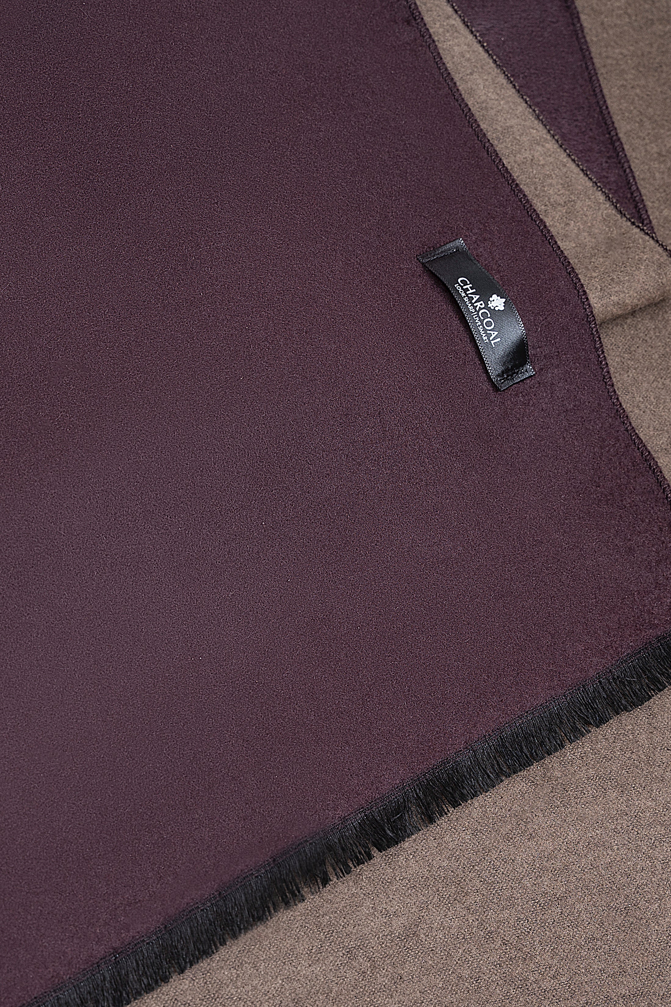 Dark purple scarf corner close-up with fringe edge and brand tag label