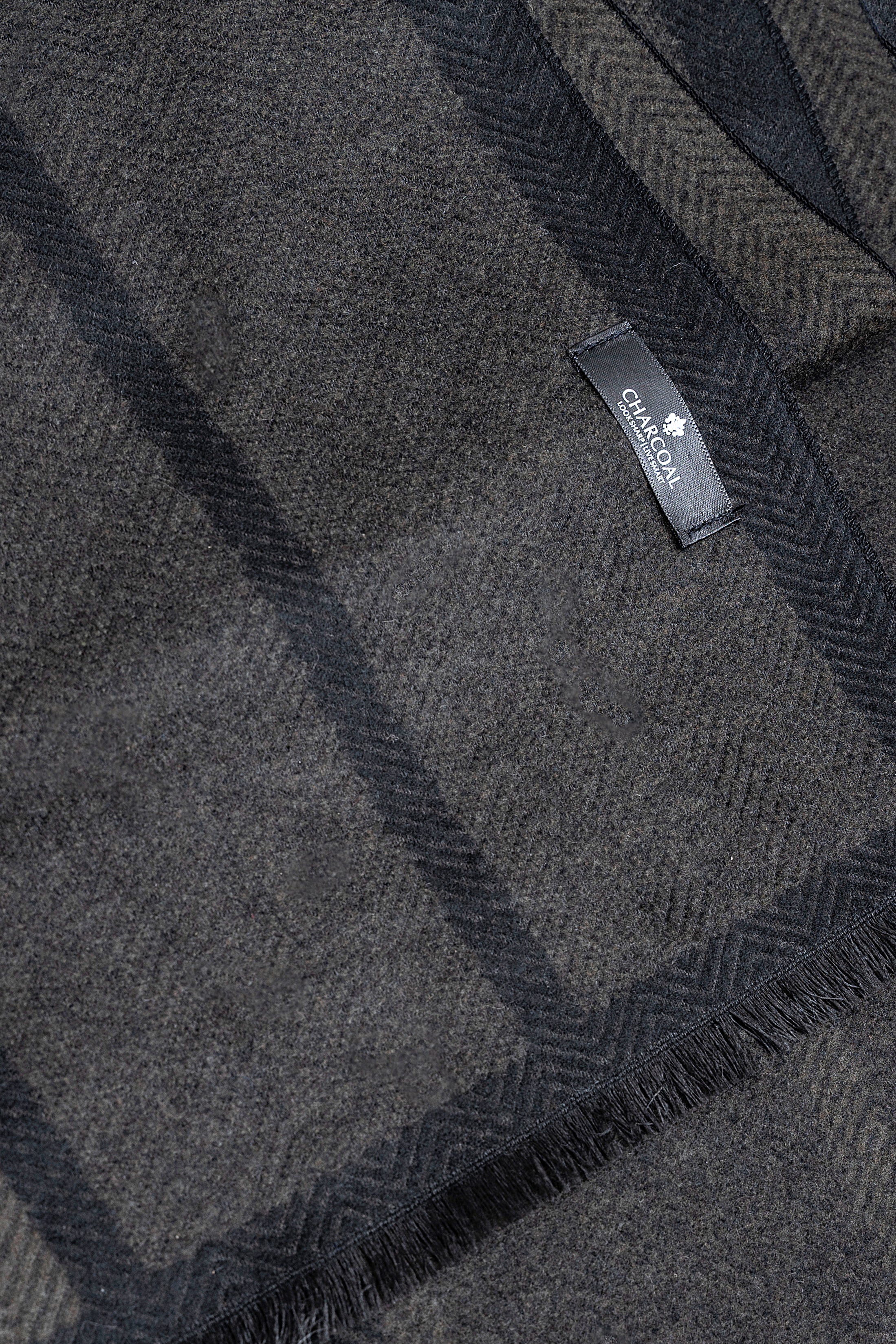 Dark plaid scarf fabric detail with fringed edge and woven label