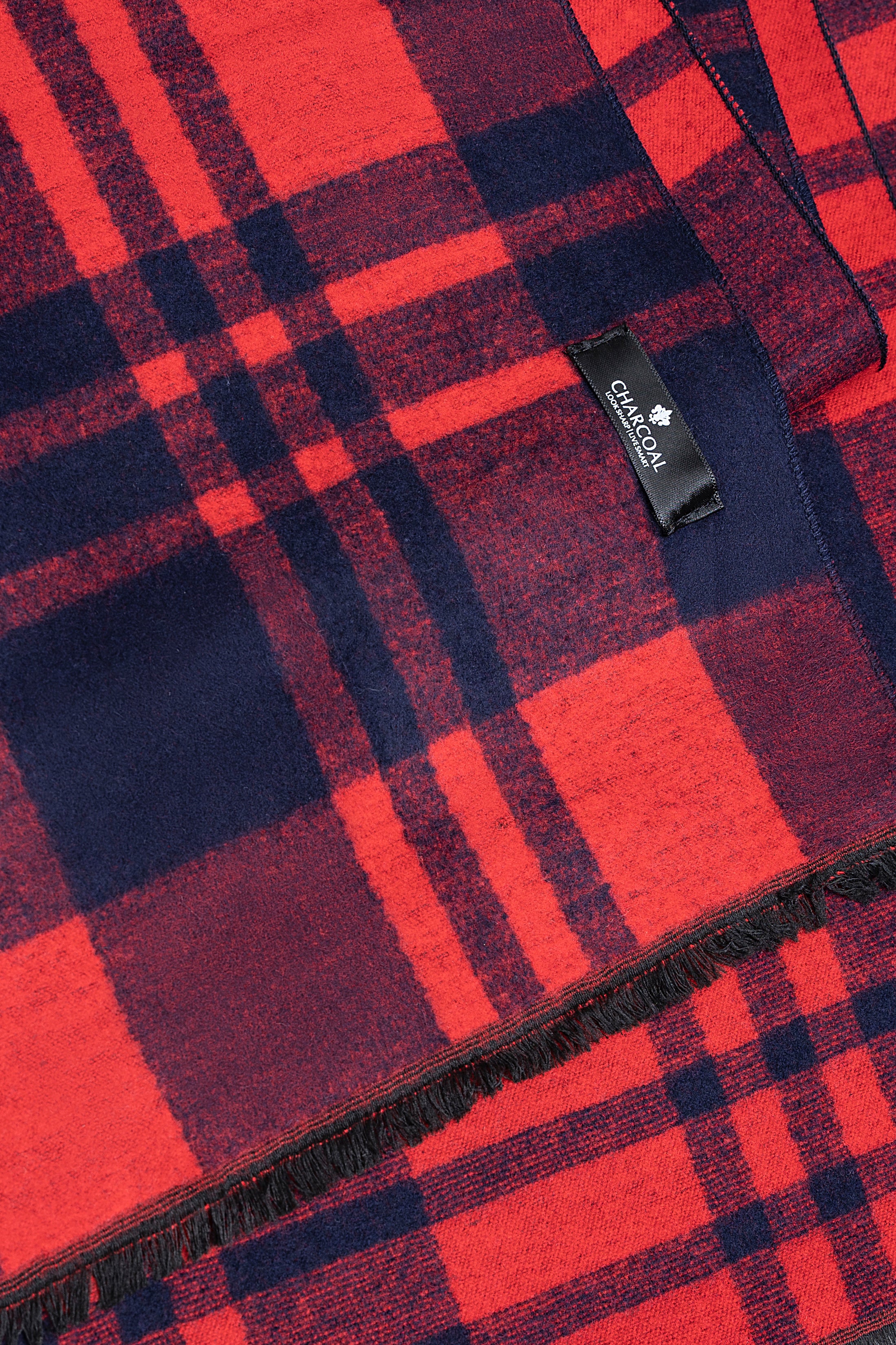 Plaid scarf corner with red and navy checks and a fabric brand label, fringed hem.