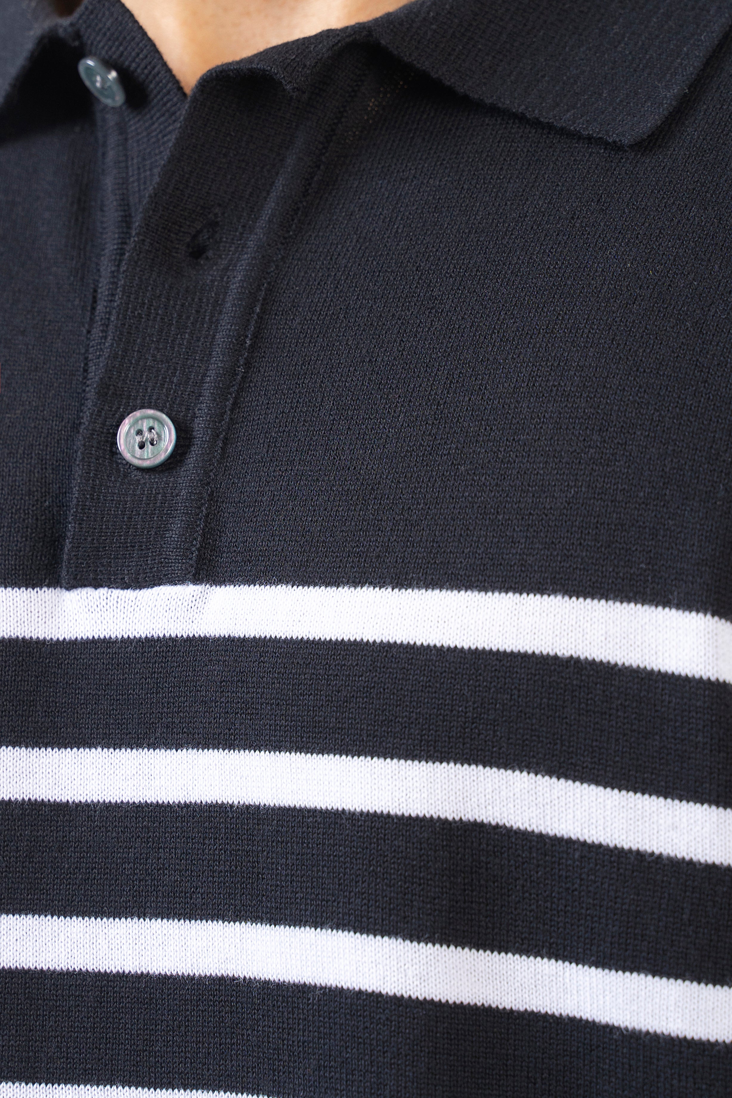 Black knit polo collar with white striped placket and button detail.