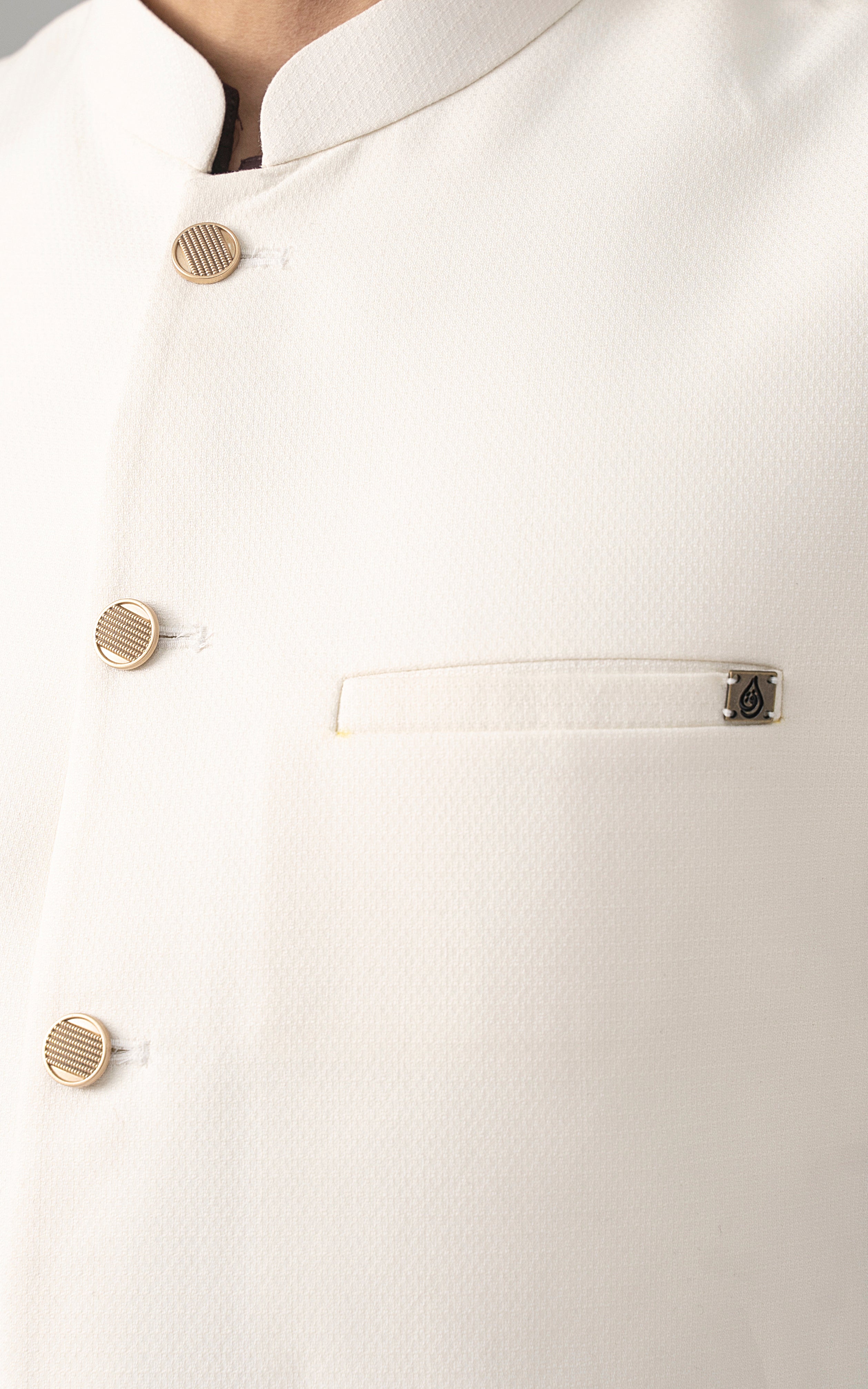 Off-white textured waistcoat detail with gold button row and chest pocket opening.