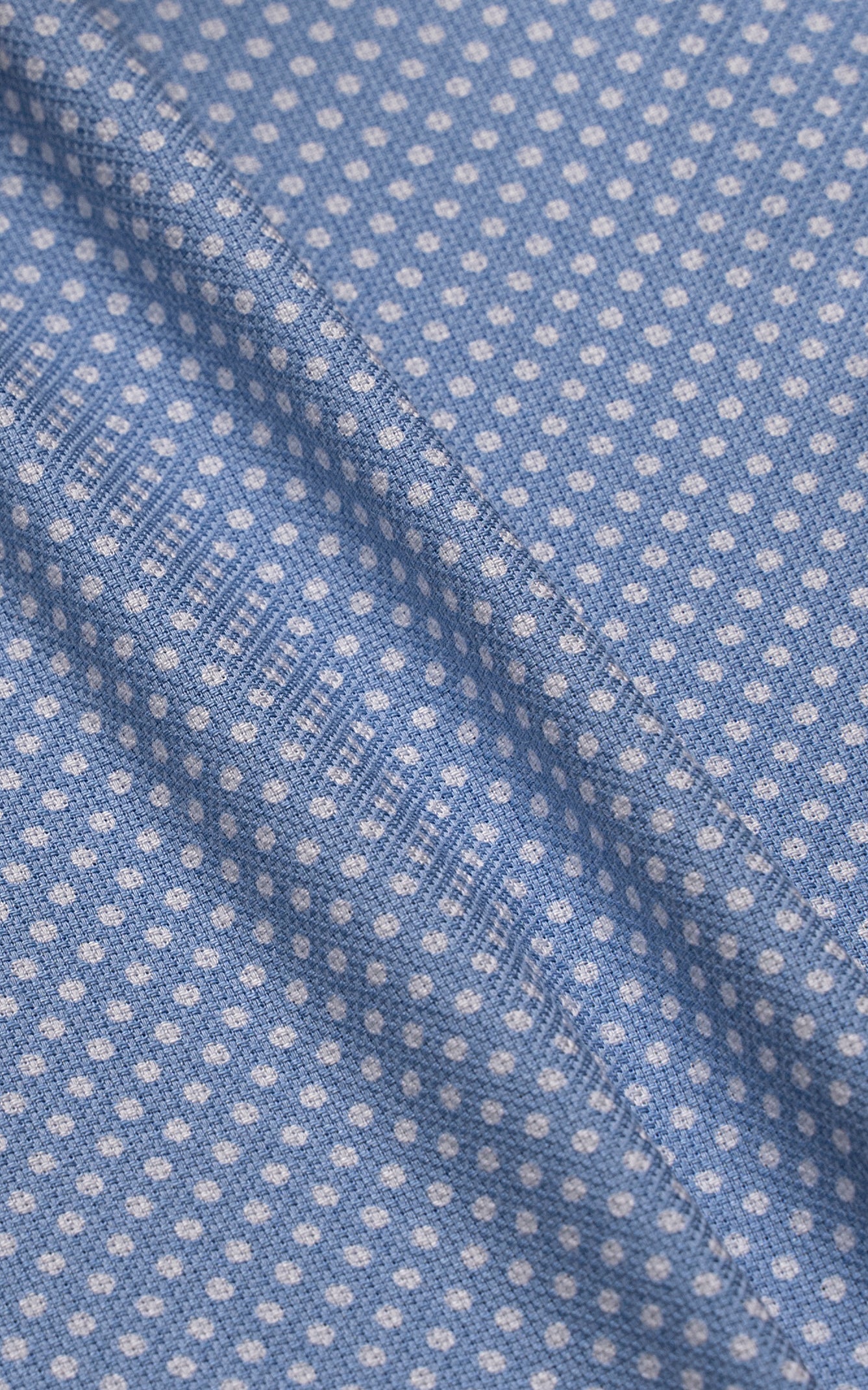 Men's blue dress shirt fabric close-up with small white dot pattern and seam details.