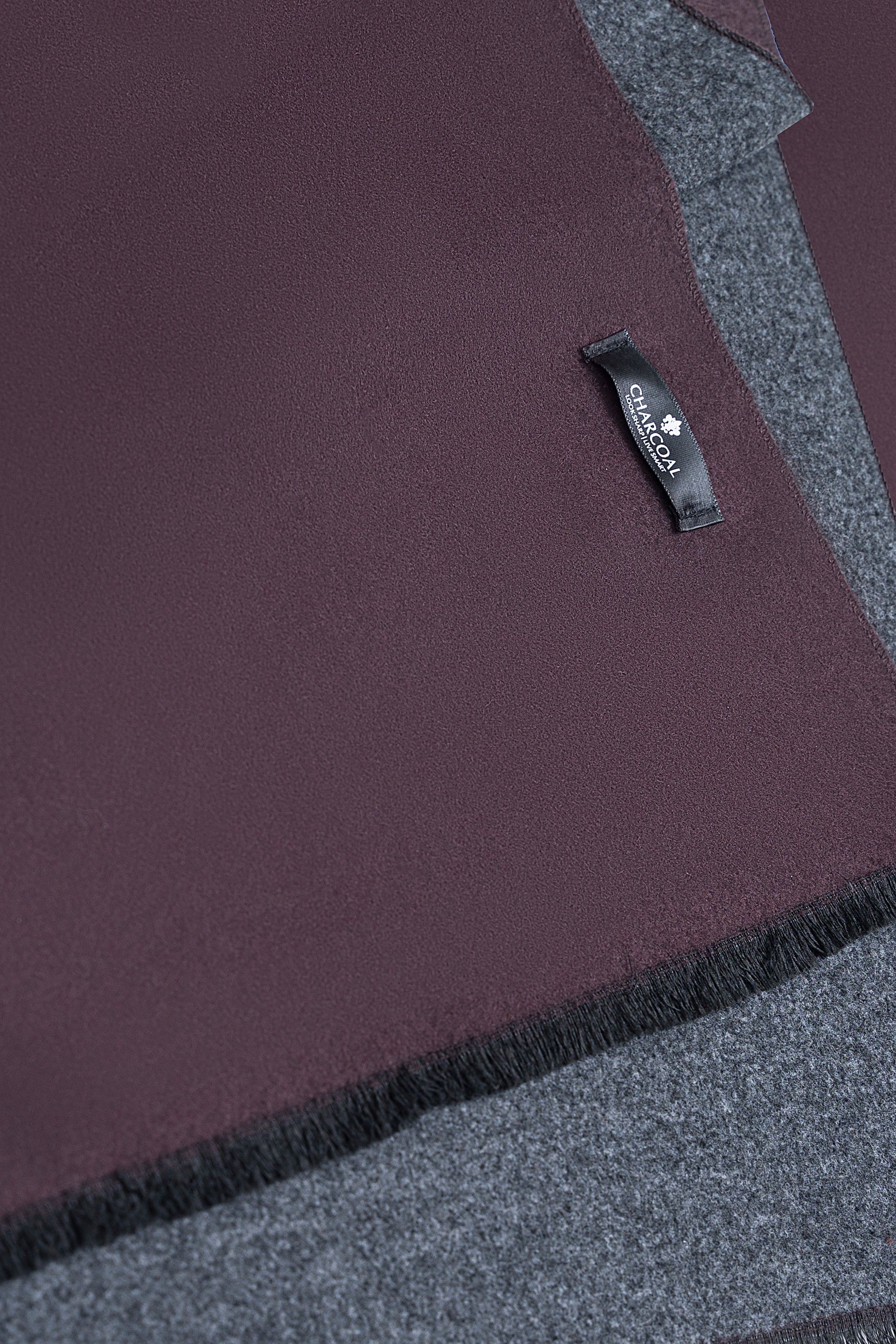 Close-up of dark maroon scarf label and short black fringe along the edge.