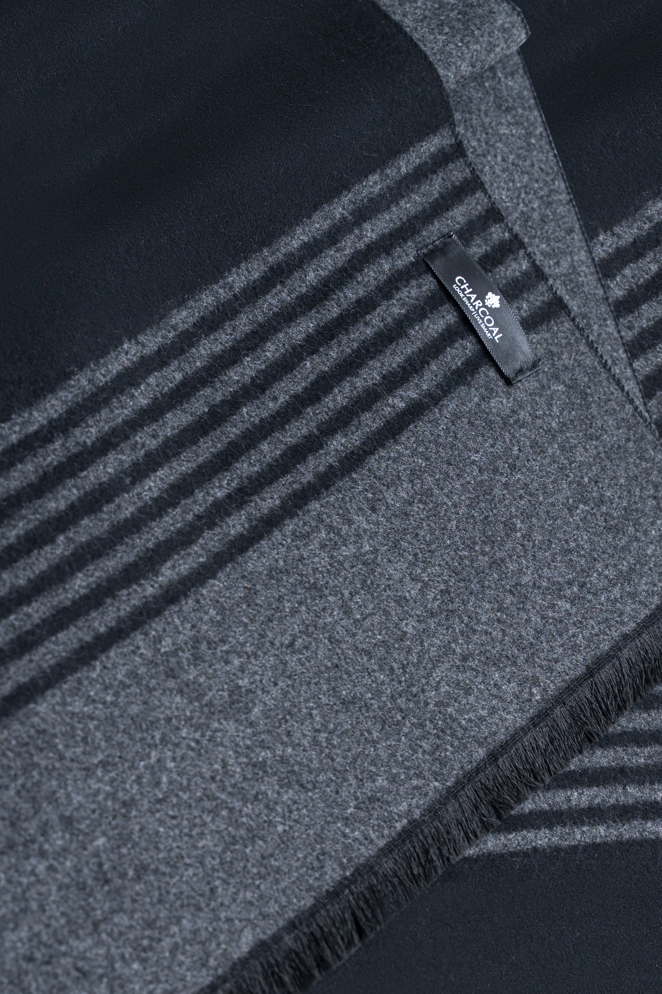 Dark scarf close-up with gray striped band and brand label near fringed hem