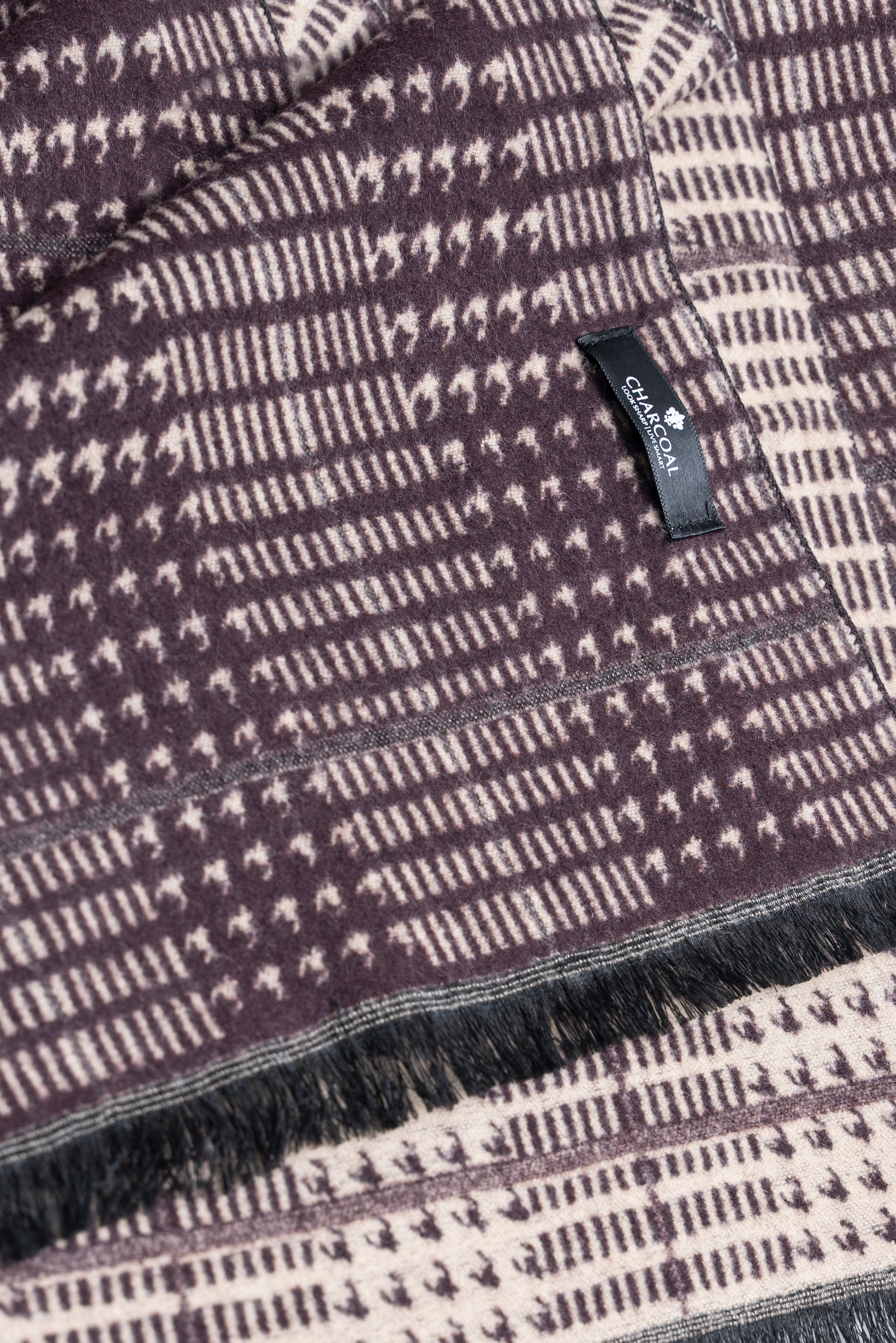 Dark scarf close-up with check grid knit, stitched label, and fringe trim