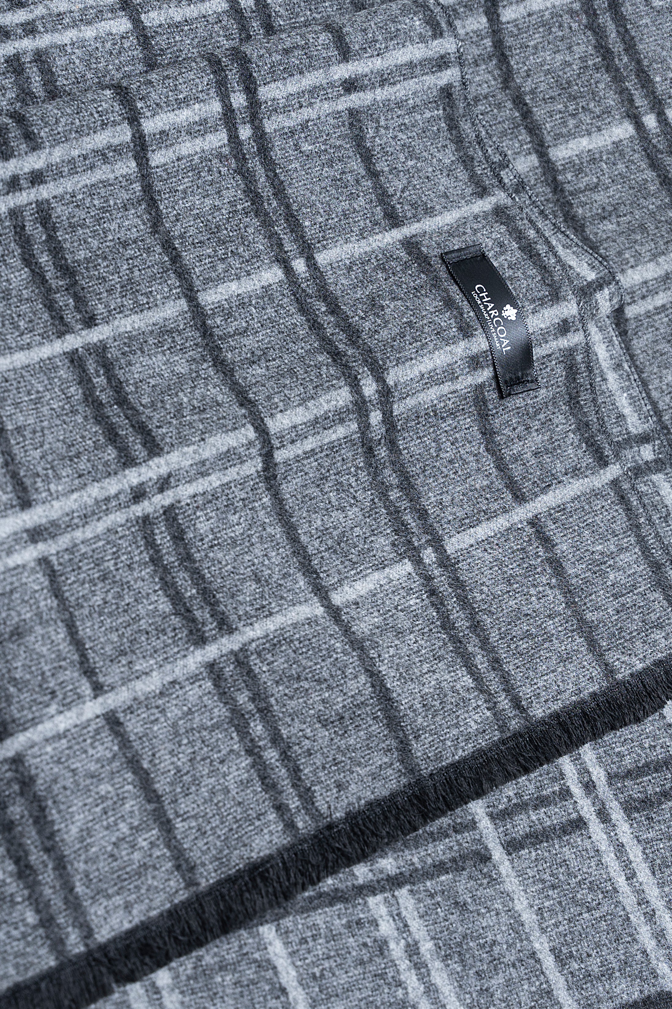 Plaid scarf close-up with woven label and frayed edge; dark blue-gray grid pattern