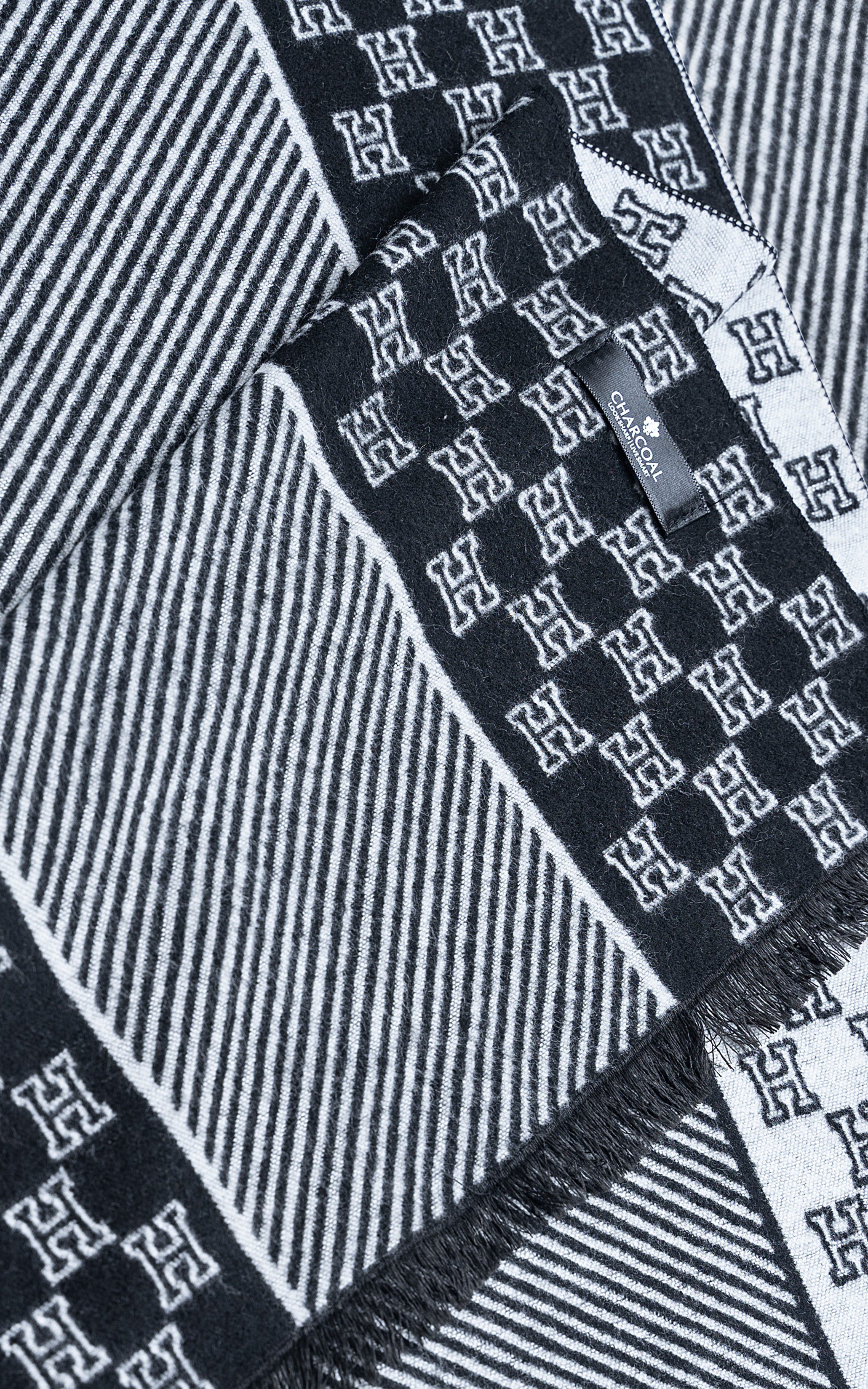 Navy patterned scarf close-up with diagonal stripes, H motifs, and fringe trim