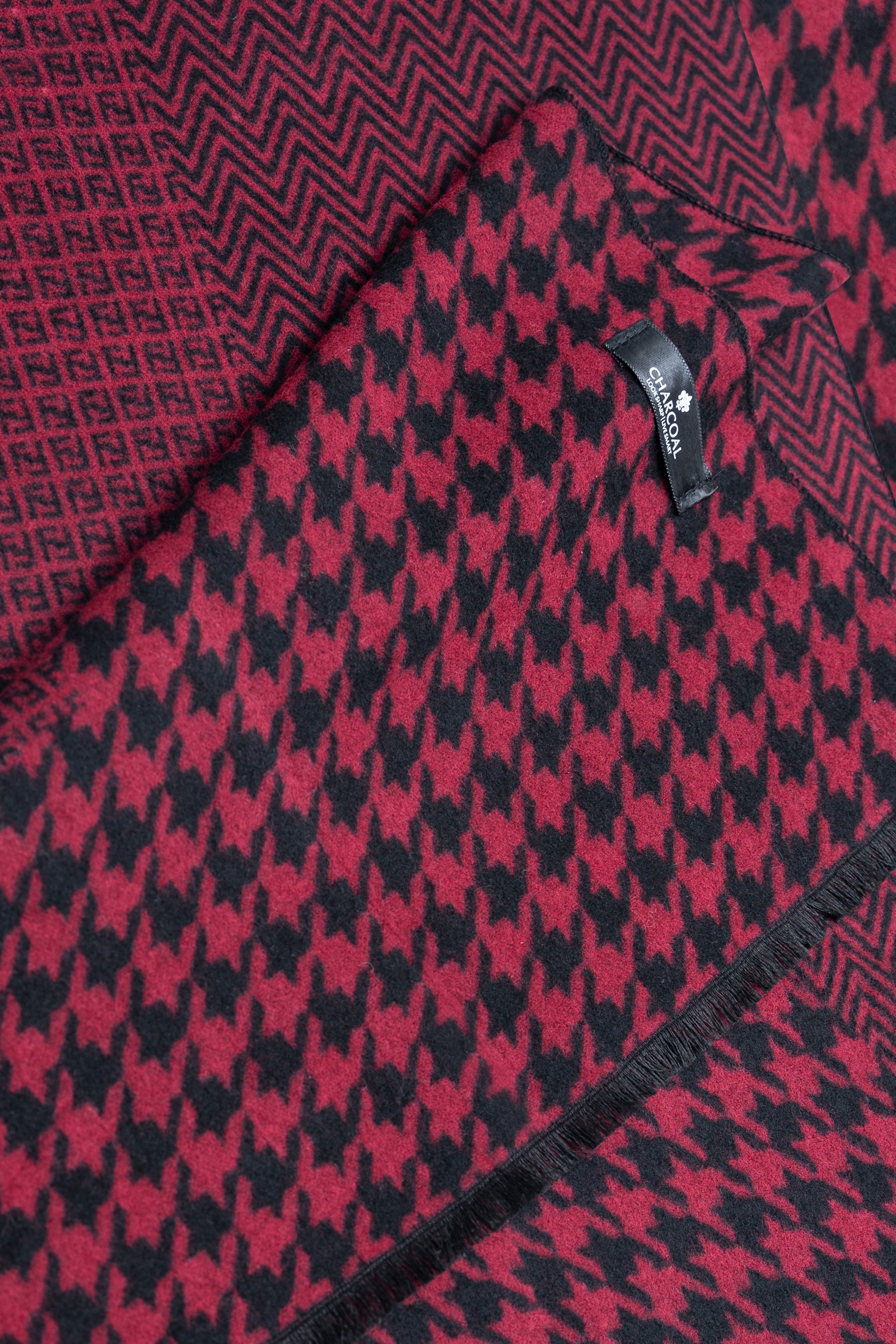 Close-up of maroon scarf with black houndstooth pattern and stitched edge.