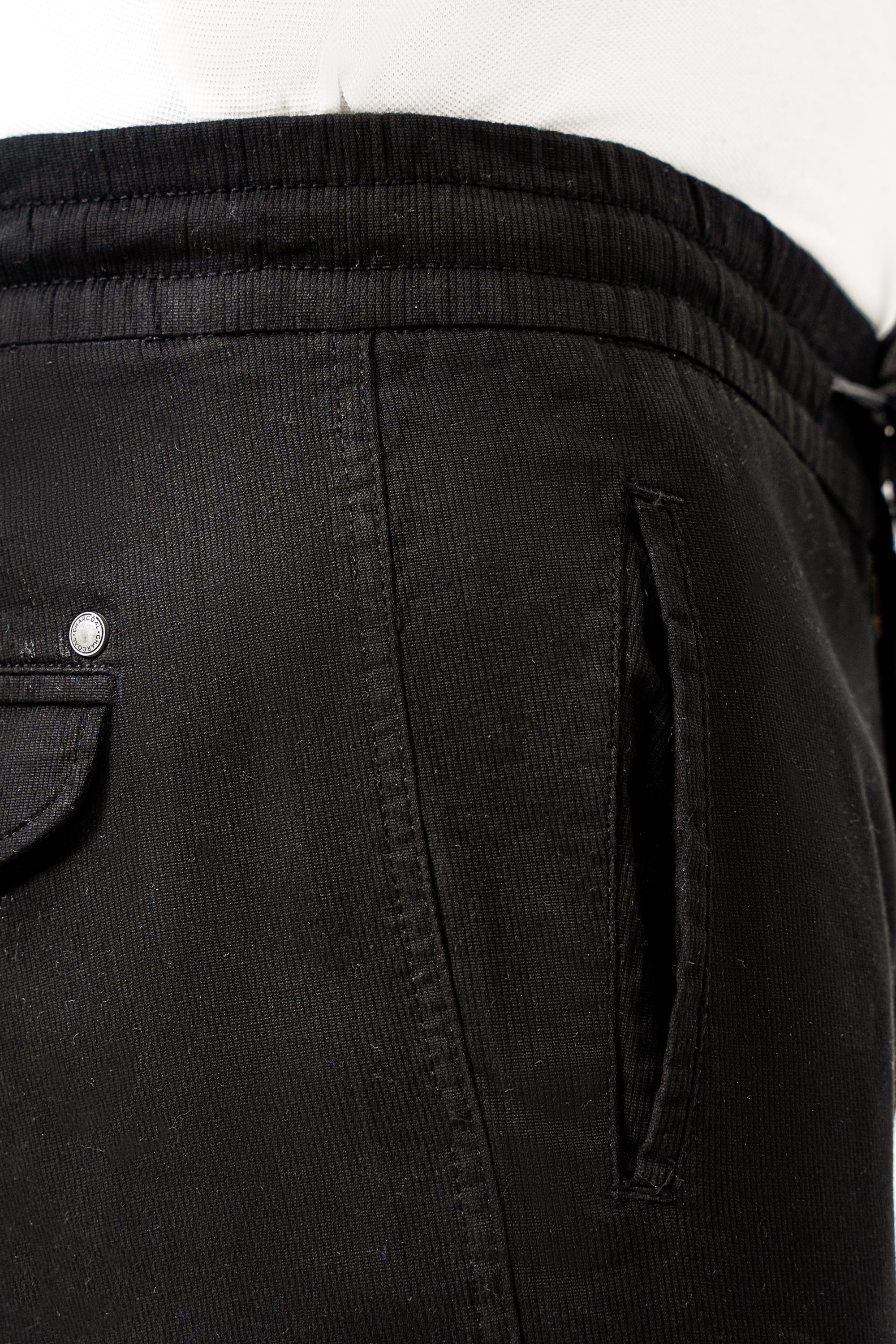 Black jogger trouser fabric close-up with buttoned front pocket