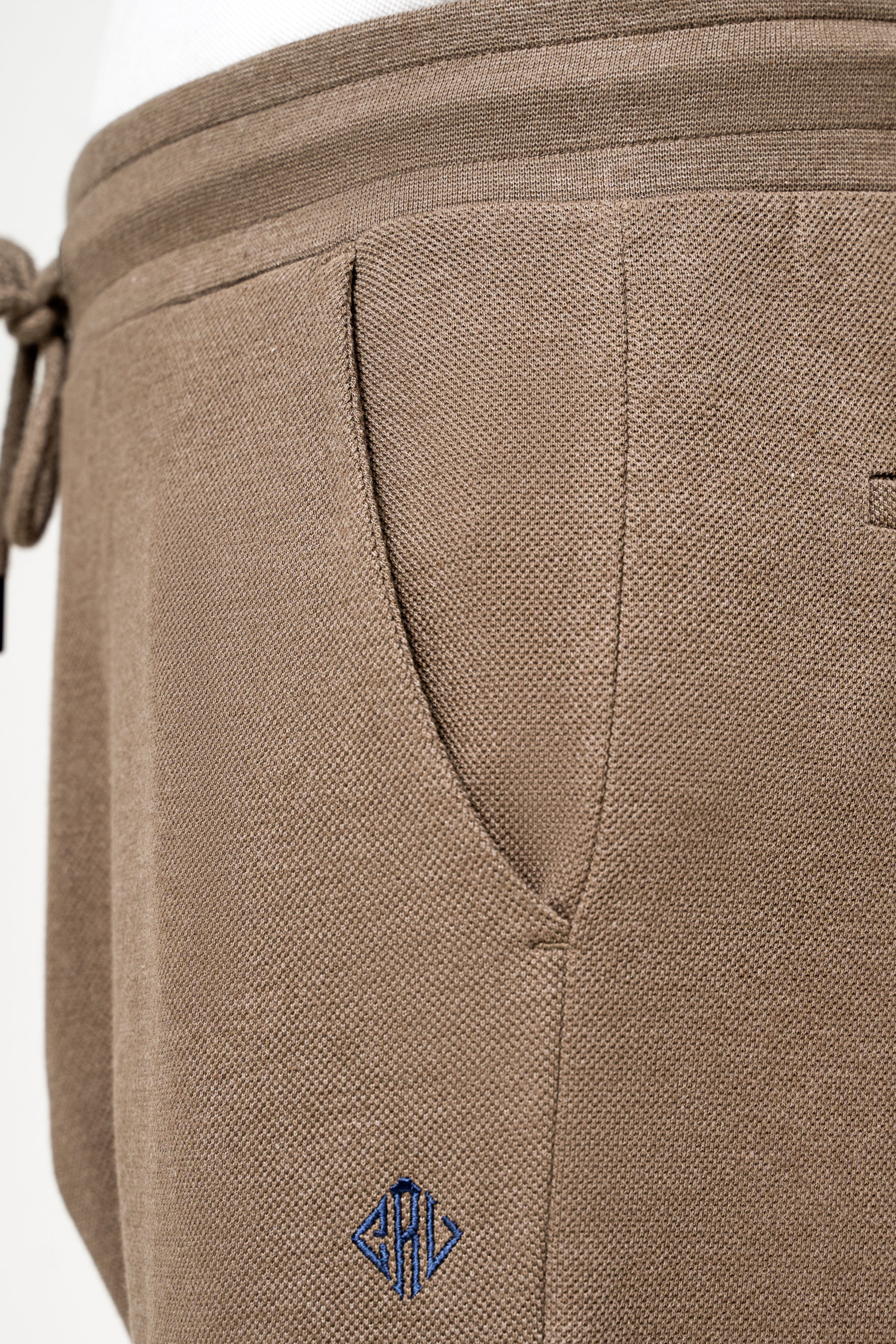 Khaki jogger trouser detail: woven fabric, logo patch, stitched pocket seam