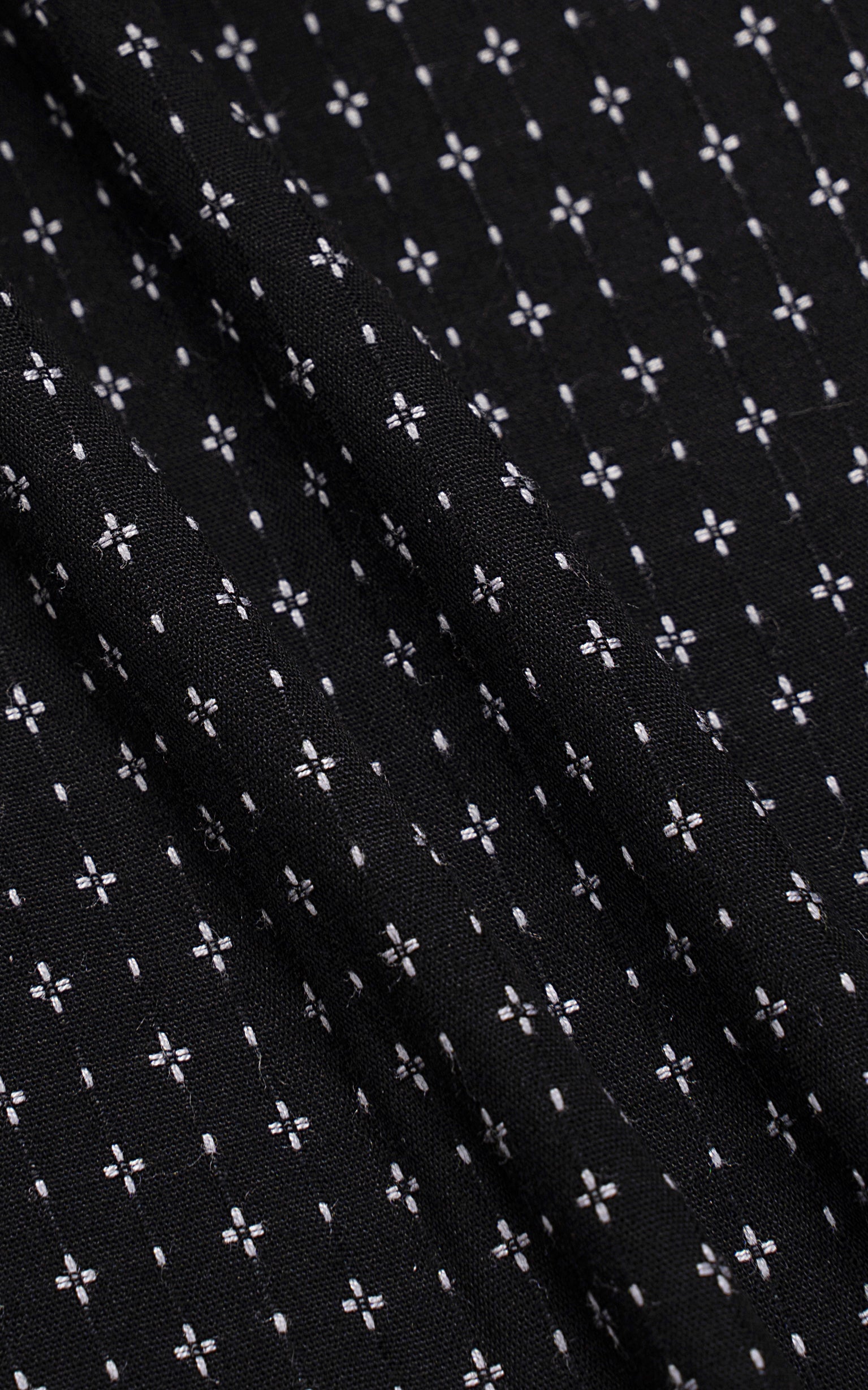 Black dress shirt fabric with small white floral pattern and textured weave.
