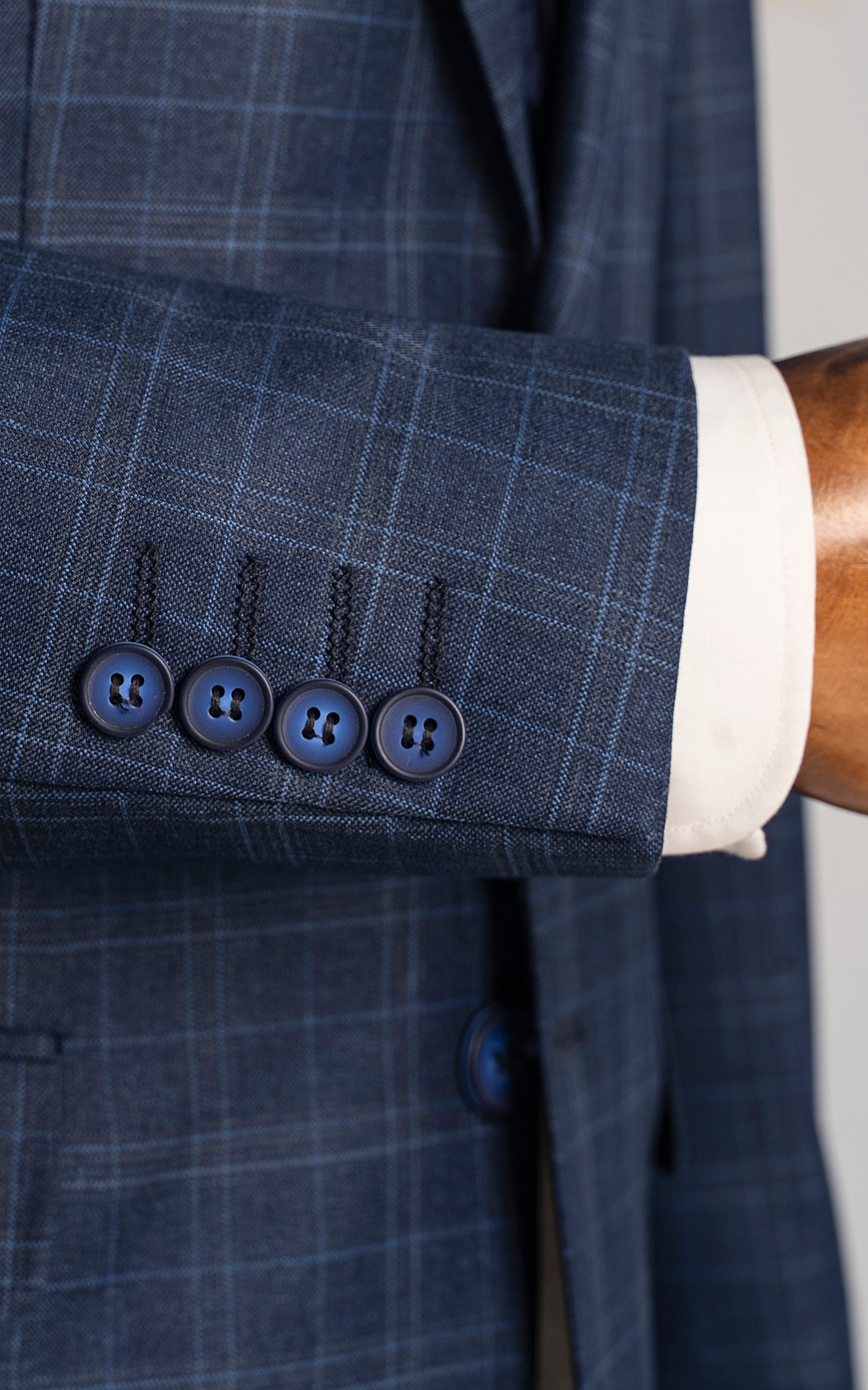 Navy blue suit sleeve cuff with four dark buttons and plaid texture