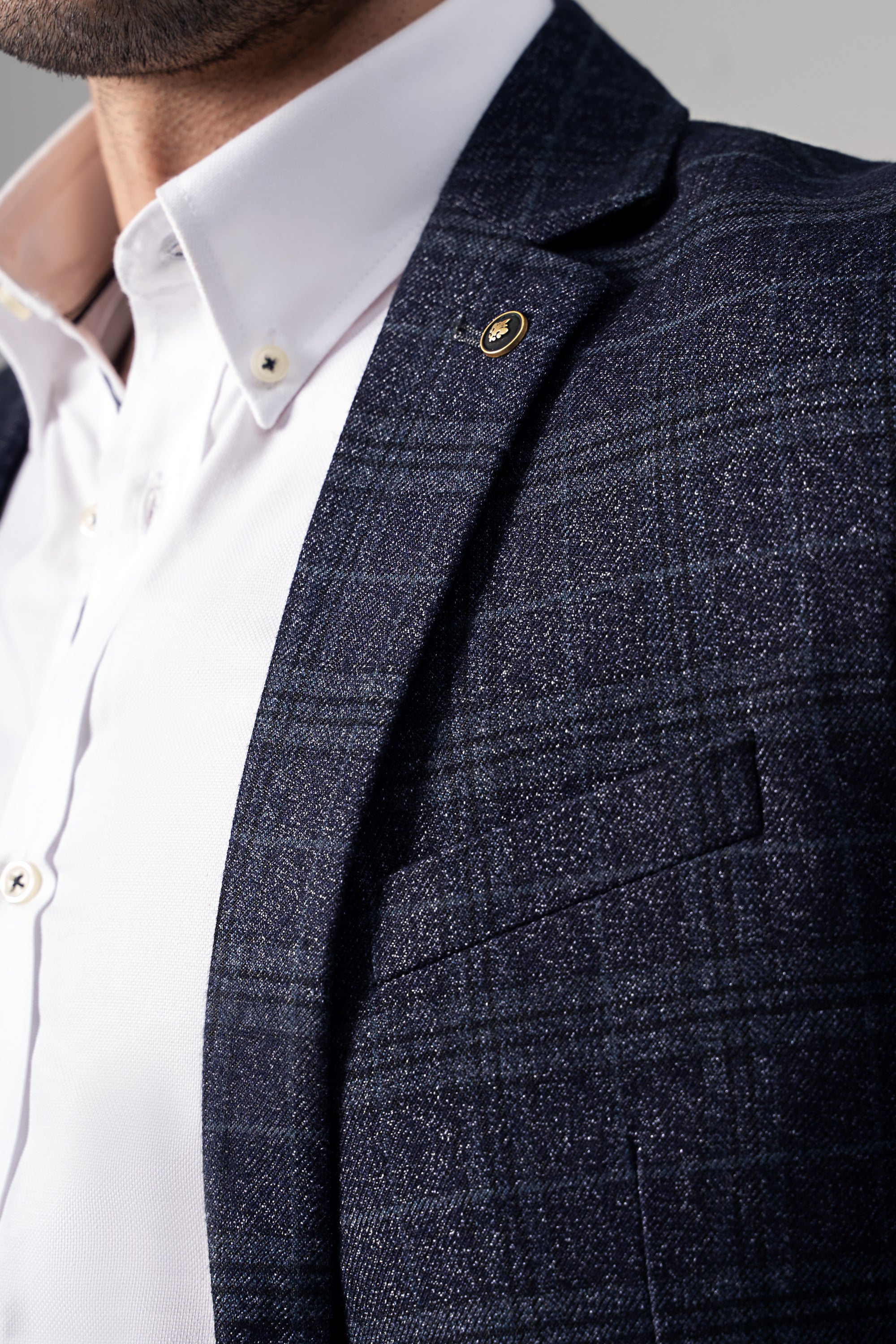 Close-up of navy casual coat lapel with gold-tone button and patterned fabric.