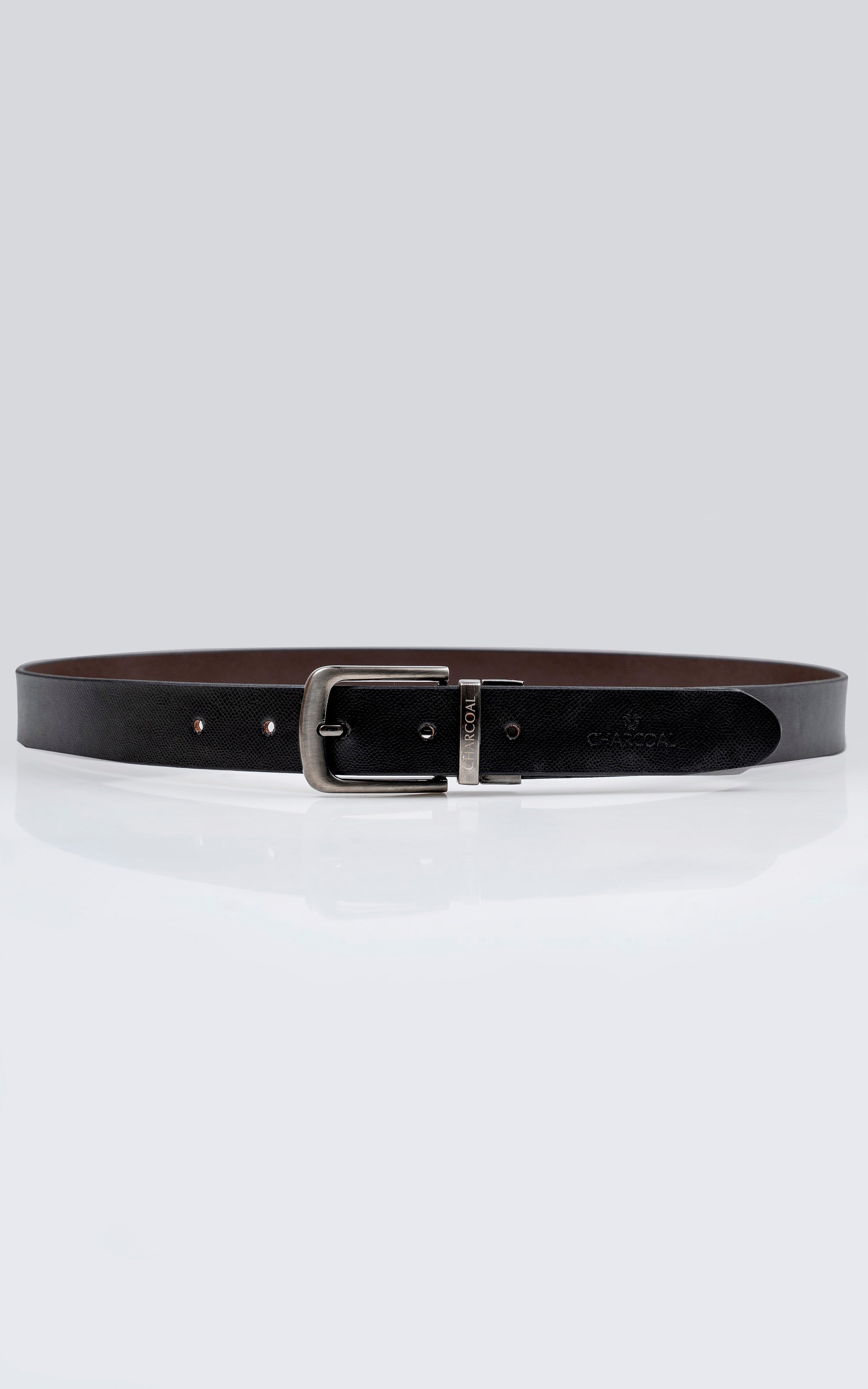 Reversible leather belt laid flat, dark side facing up with silver rectangular buckle.