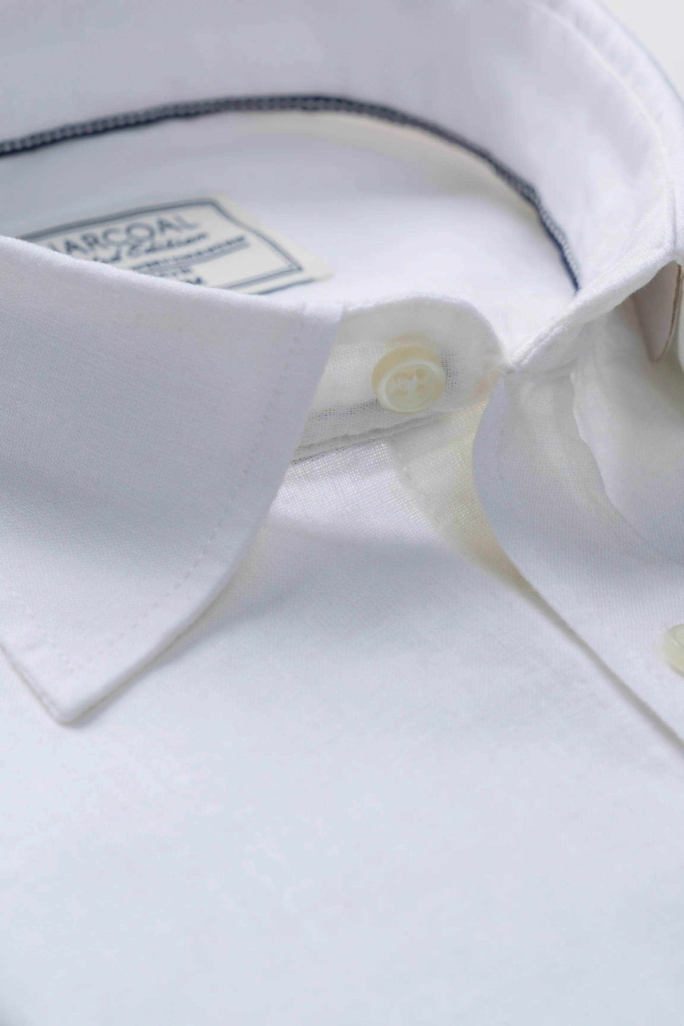 White linen shirt collar close-up with logo tag and gold-tone front buttons