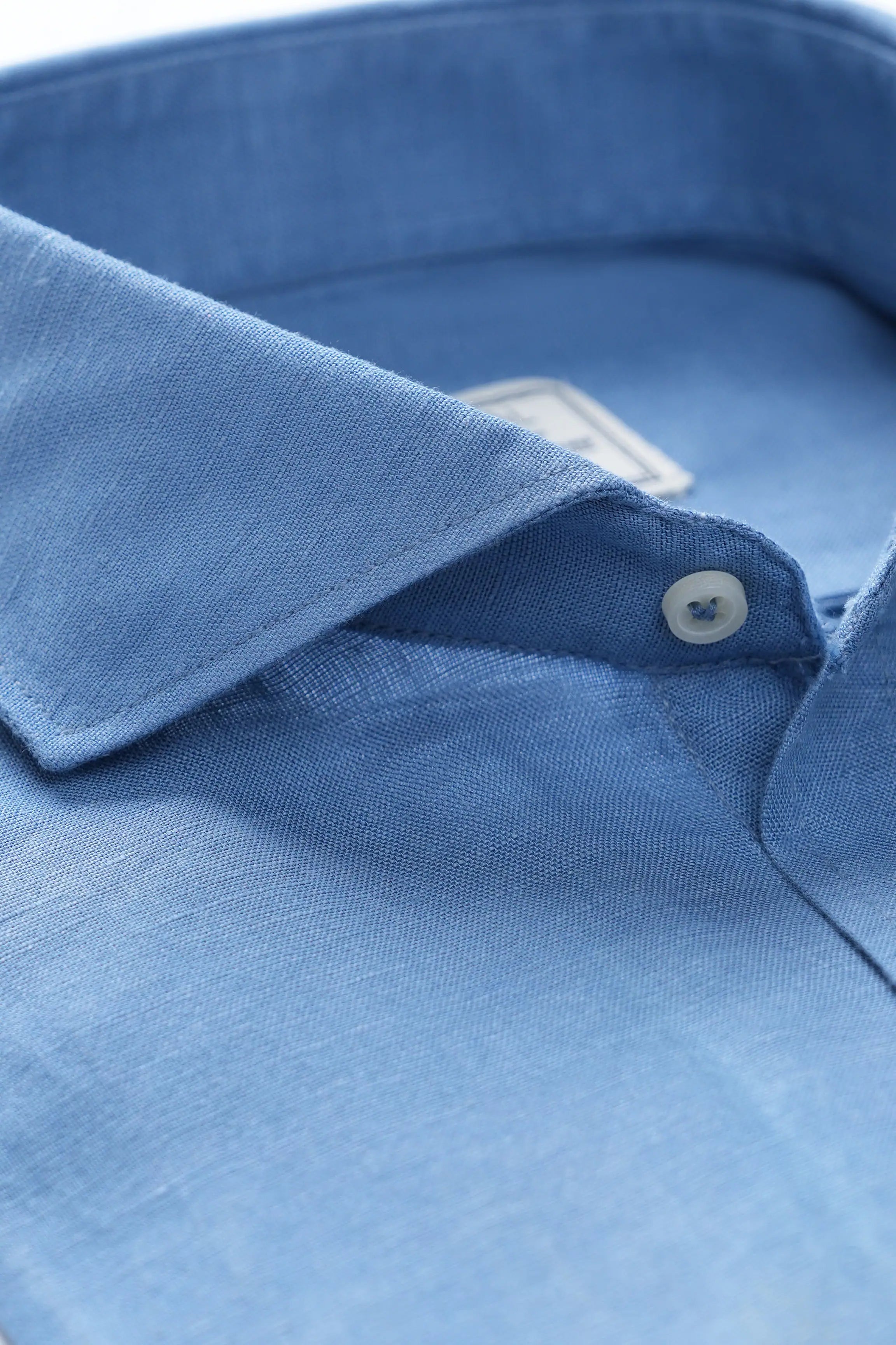 Greyish blue linen shirt collar close-up with white button and wide-spread cut