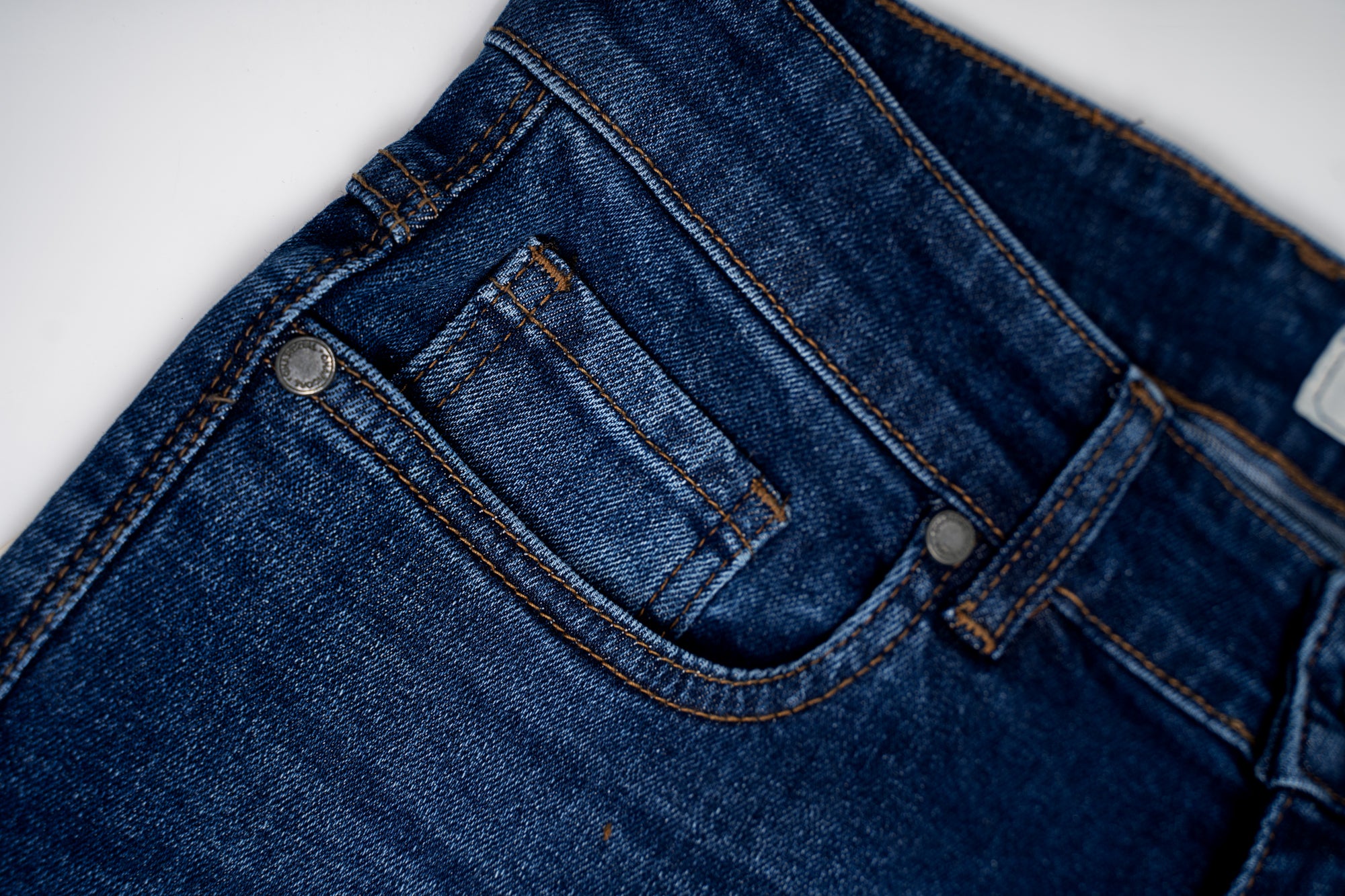 Mid blue denim jeans front pocket with curved yoke stitching and metal rivets