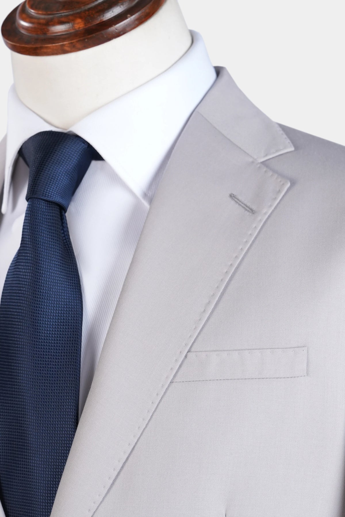 Close-up of stone gray lapel, welt pocket, and navy textured tie