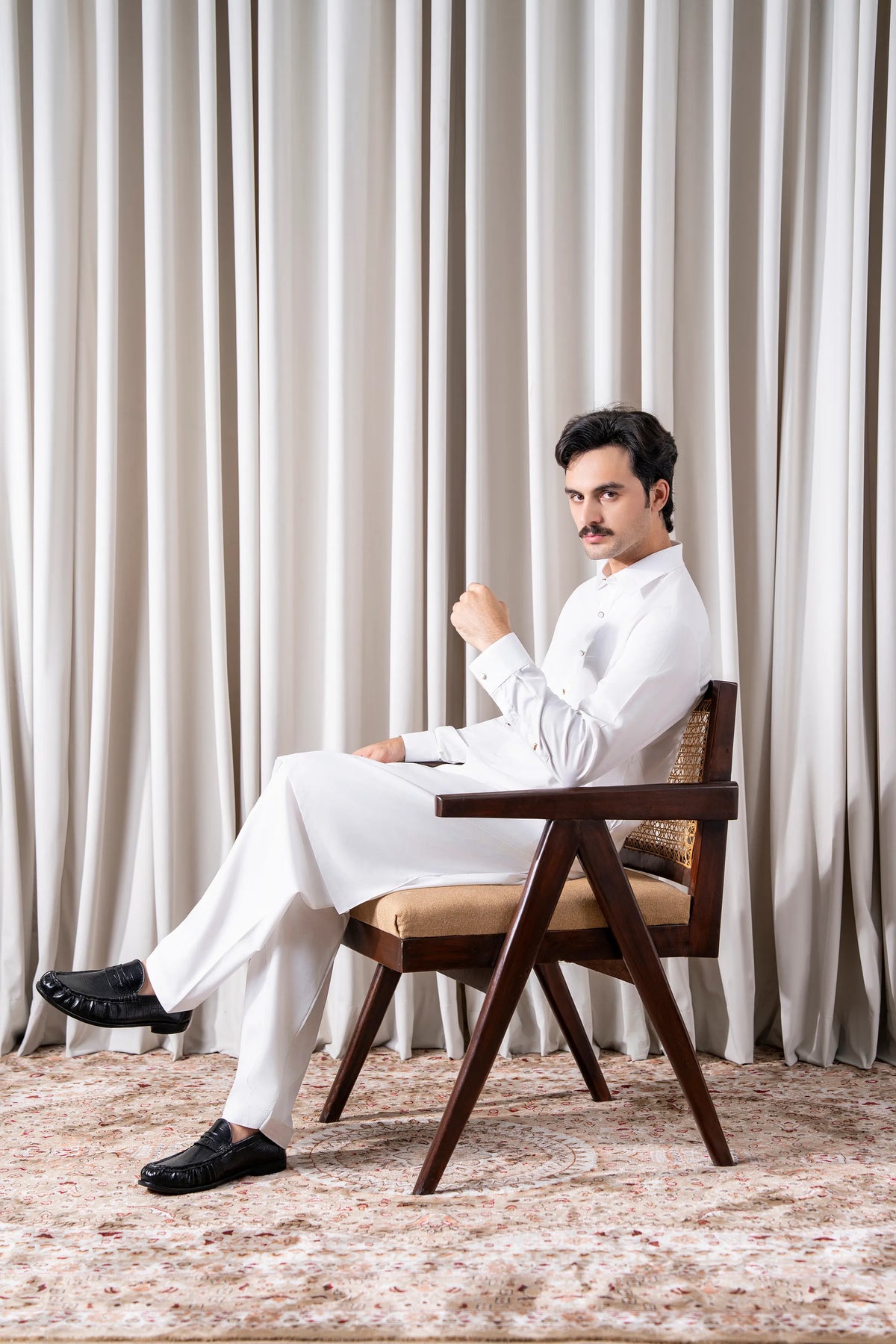 White kameez shalwar set seated on chair, long tunic with matching shalwar