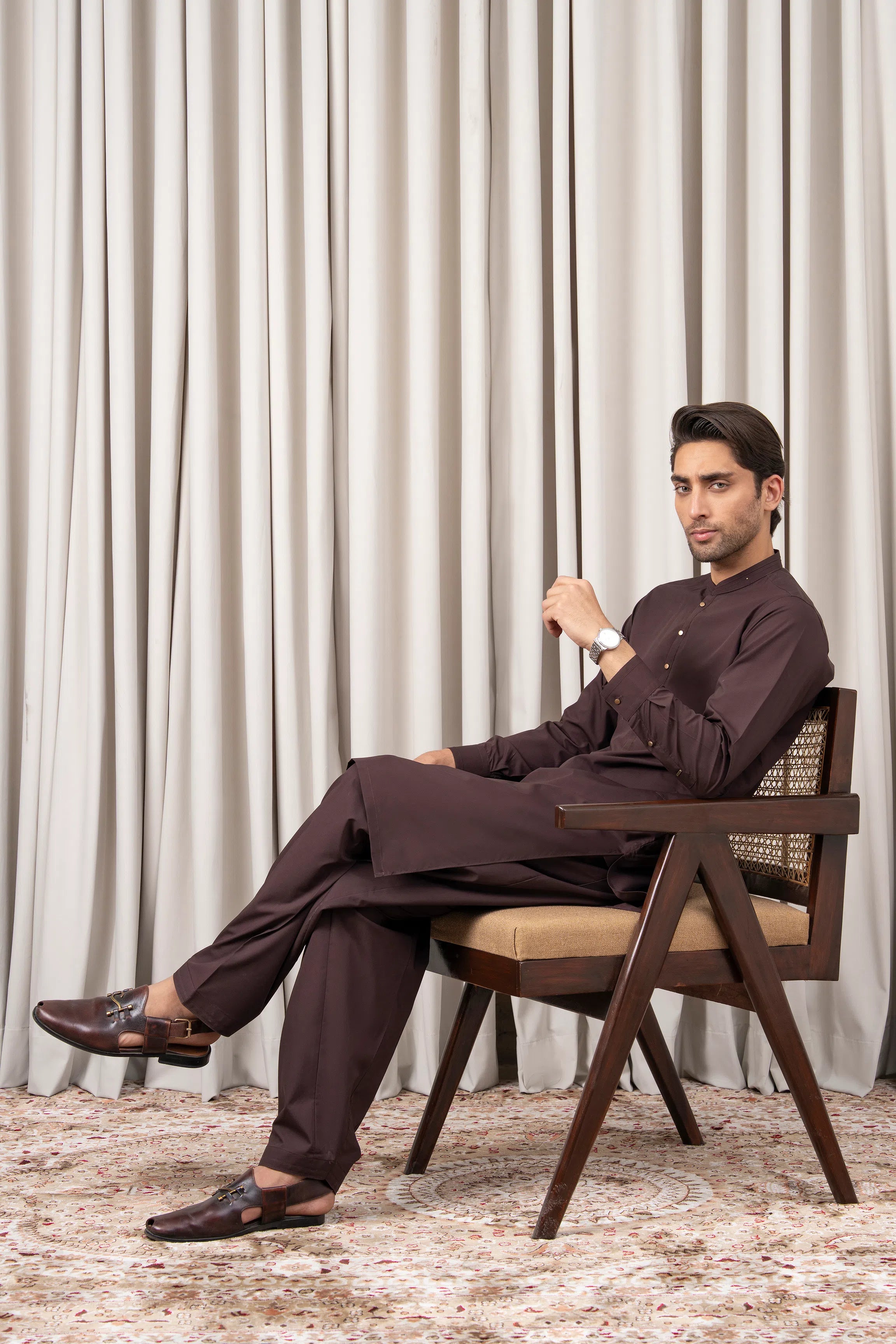 Men's dark brown kameez shalwar set with long kurta and trousers, seated pose