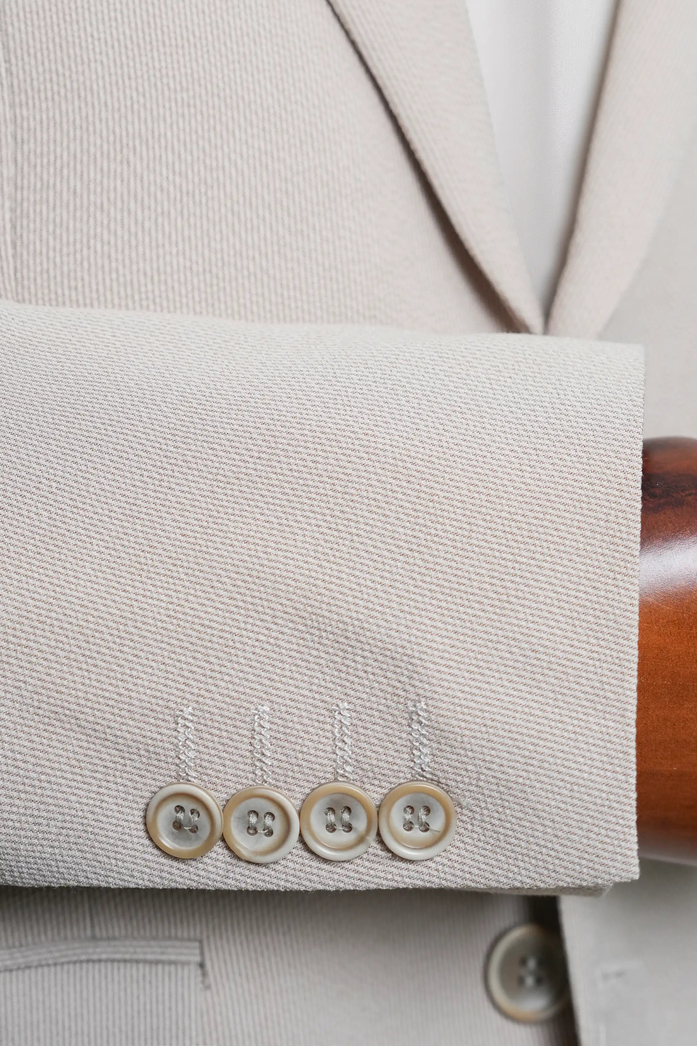 Beige coat sleeve cuff with four light buttons and stitched hem