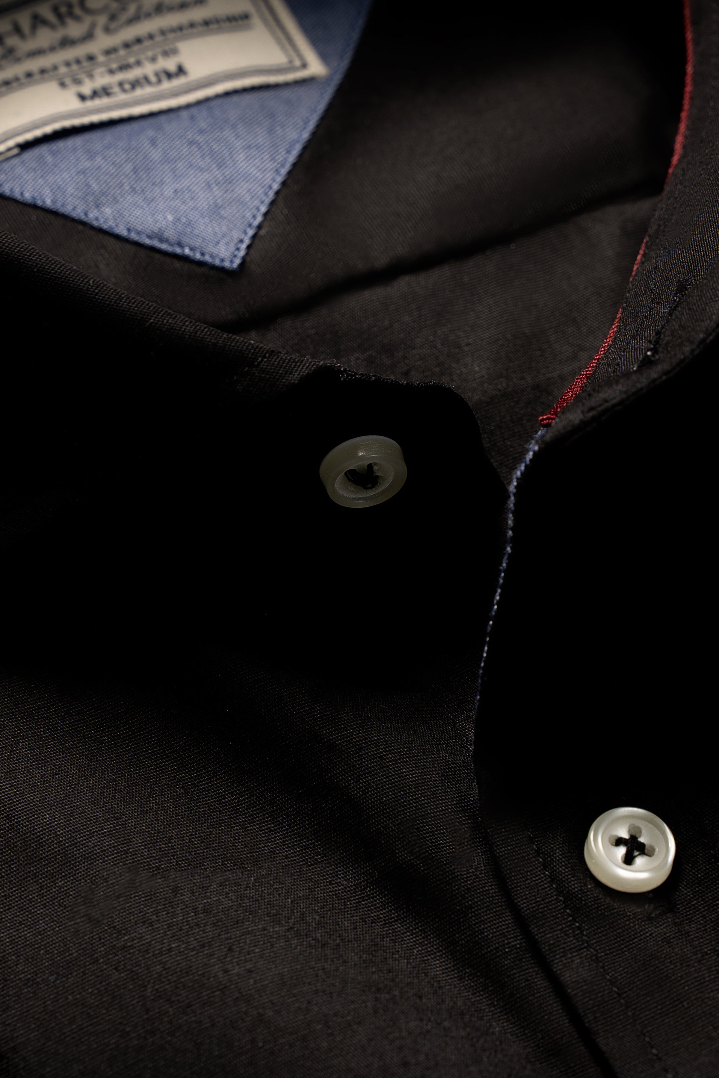 Limited edition black shirt closeup: dark button, collar label, red stitch on seam