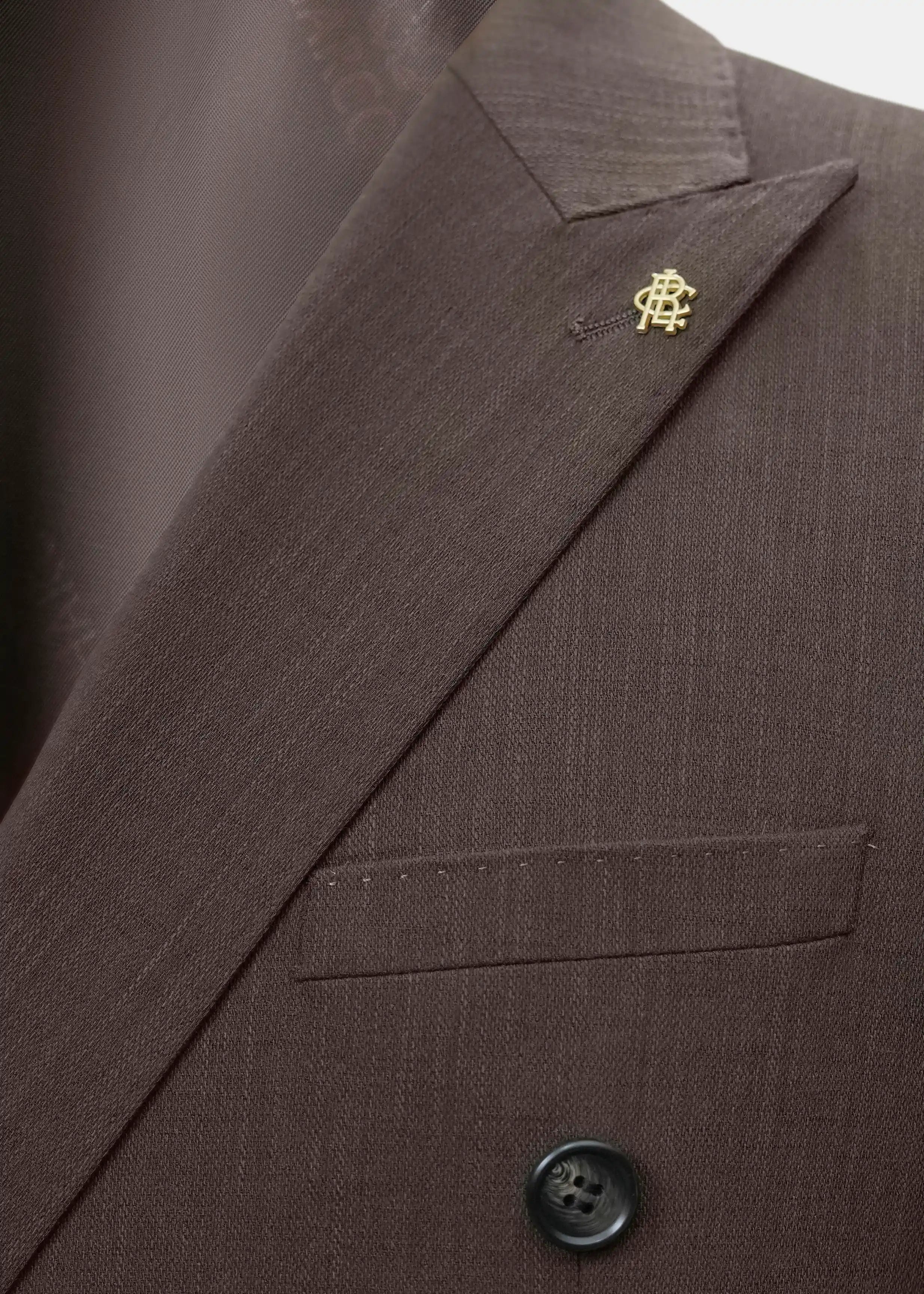 Brown coat lapel with small embroidered emblem and welt pocket detail