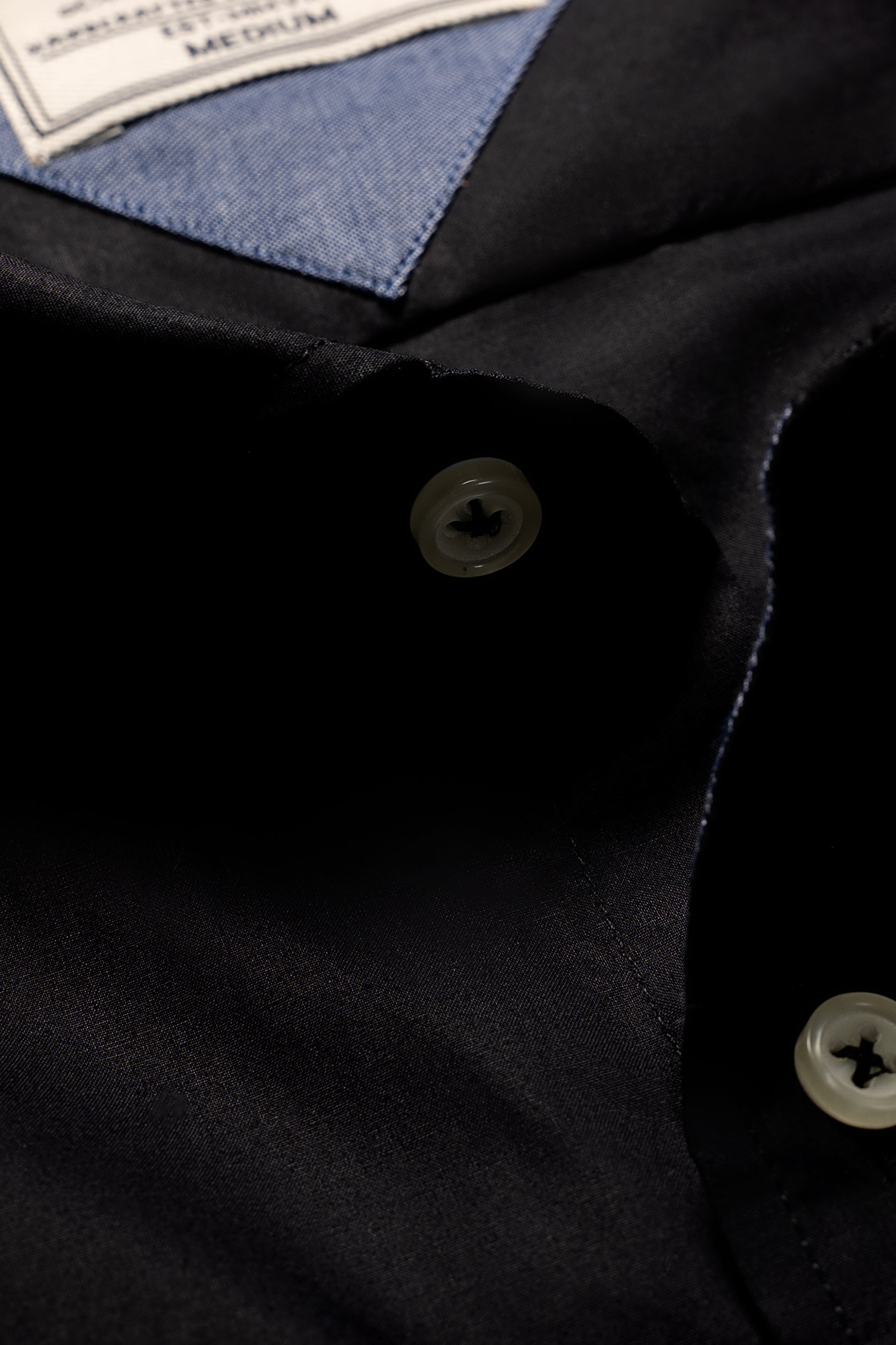 Black shirt button placket close-up with part of inner label