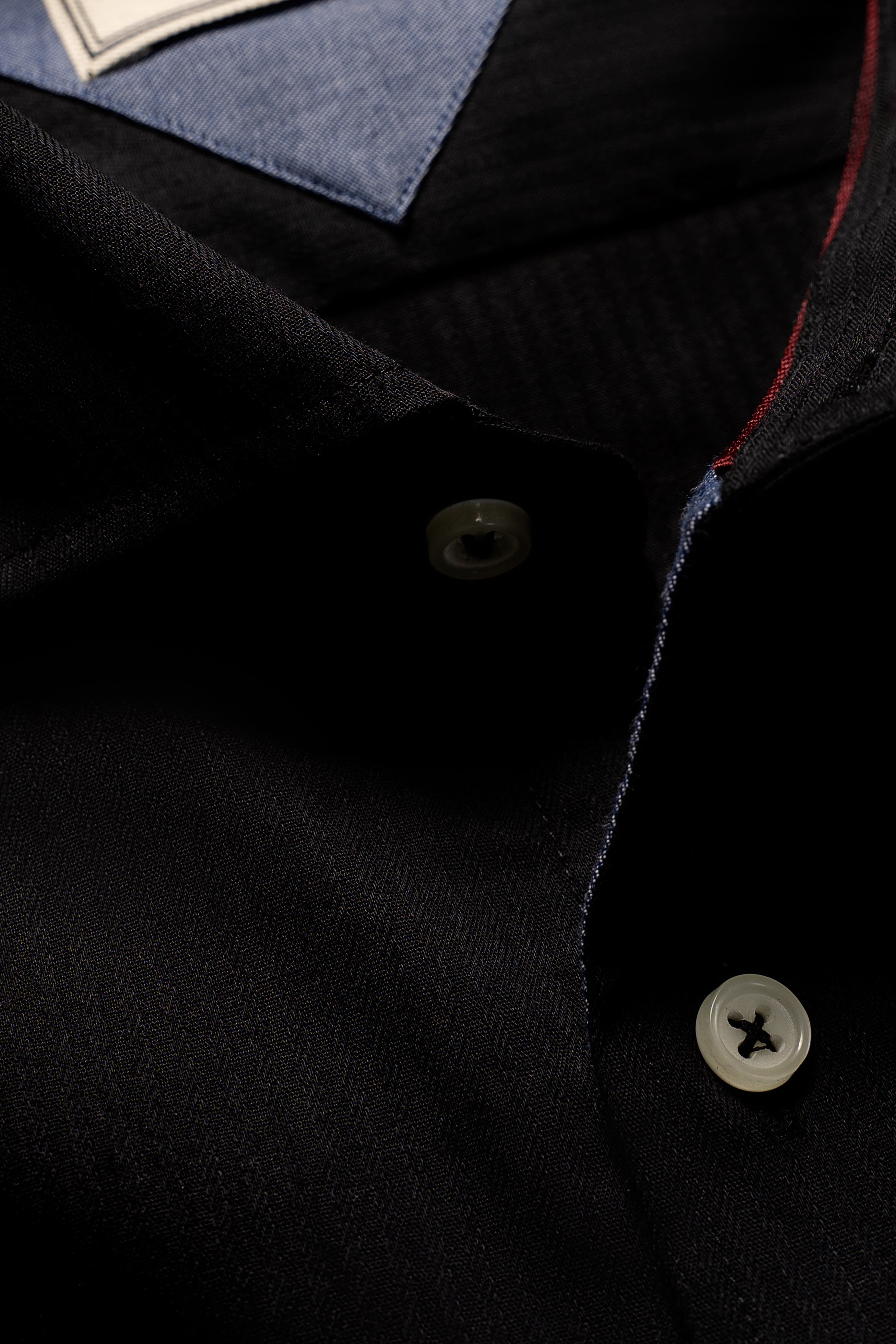 Black dress shirt detail with top button, stitched placket, and red trim