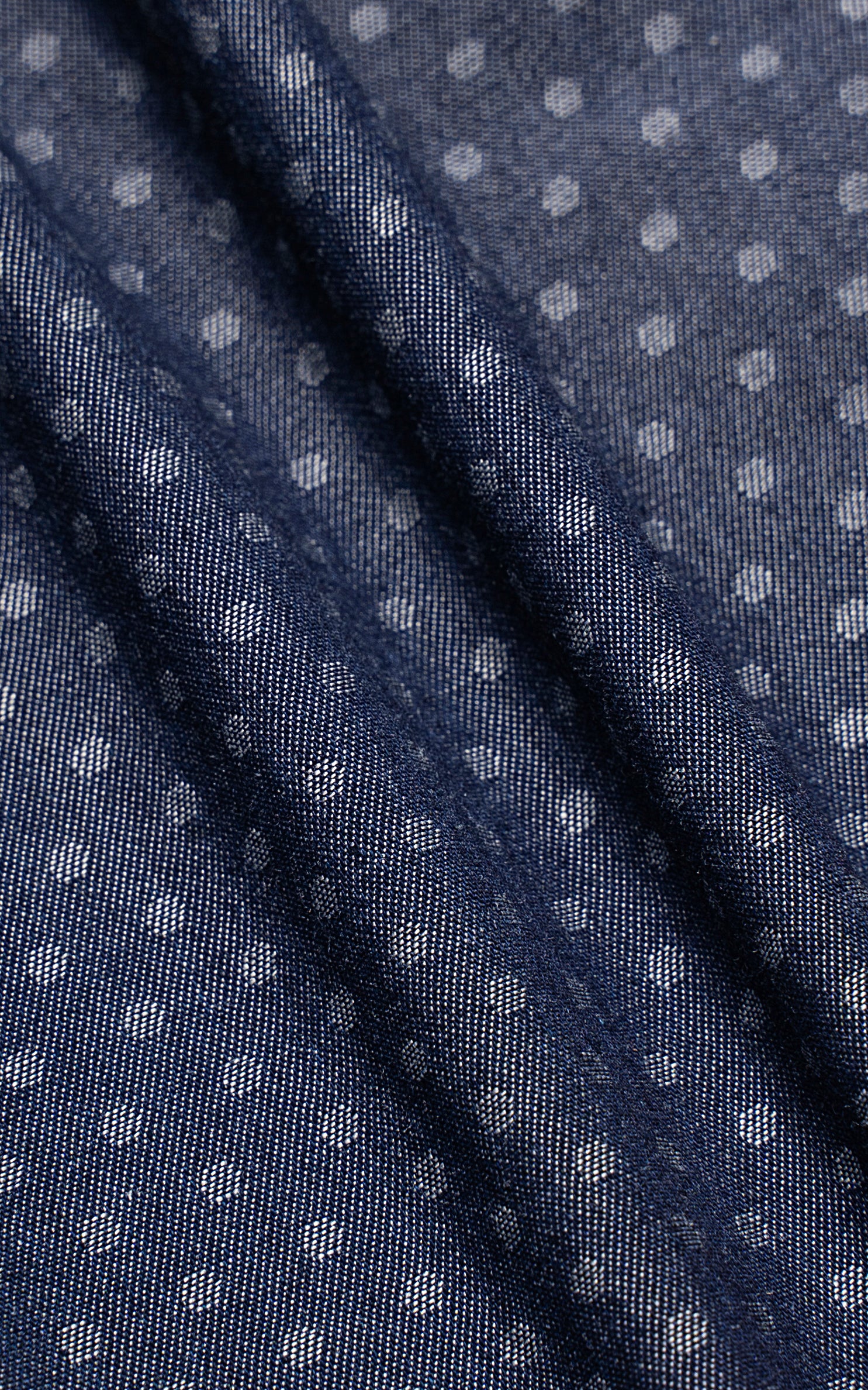 Denim blue shirt fabric detail with diagonal textured stripes over white dots