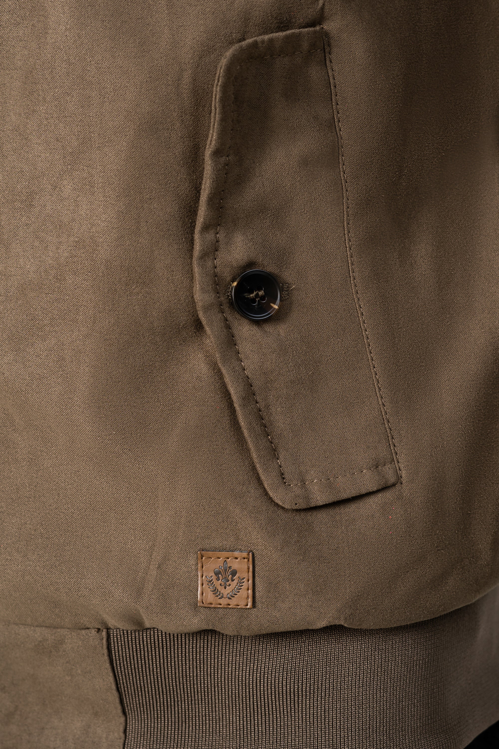 Olive suede jacket close-up: snap flap pocket, stitched panel, brand patch