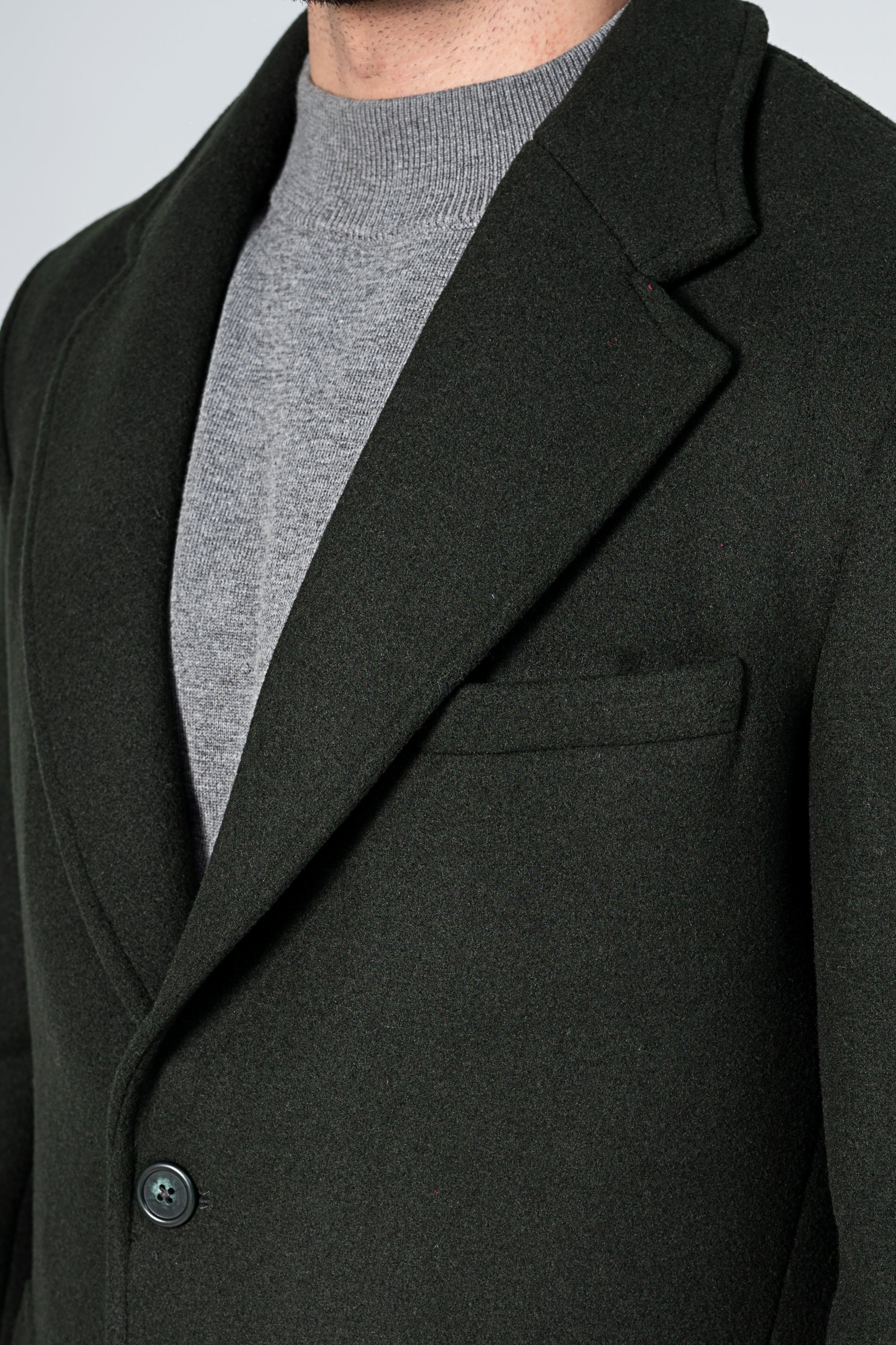 Dark green wool coat lapel and single front button with inner grey shirt visible