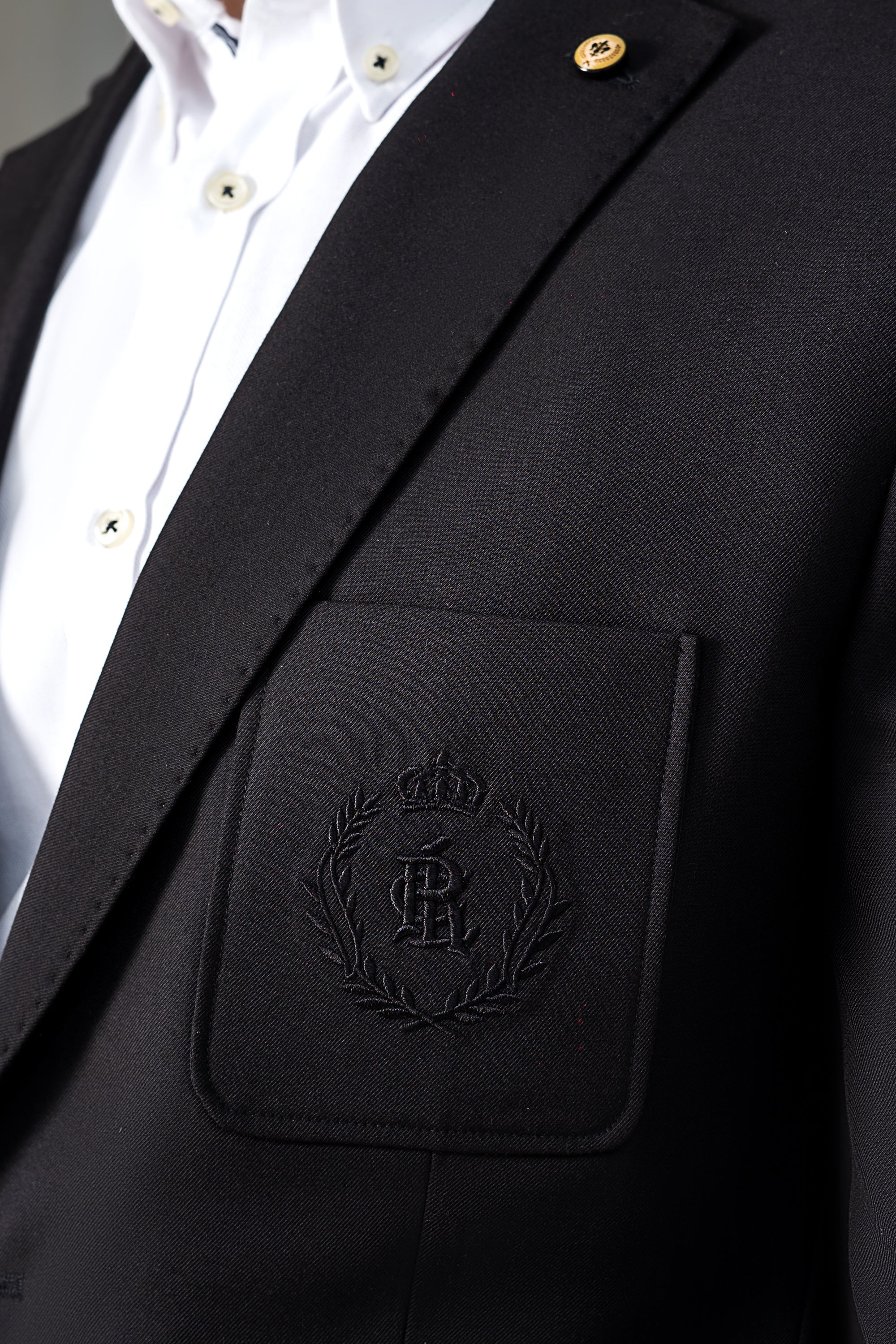 Black coat breast pocket with embossed crest and gold button on lapel