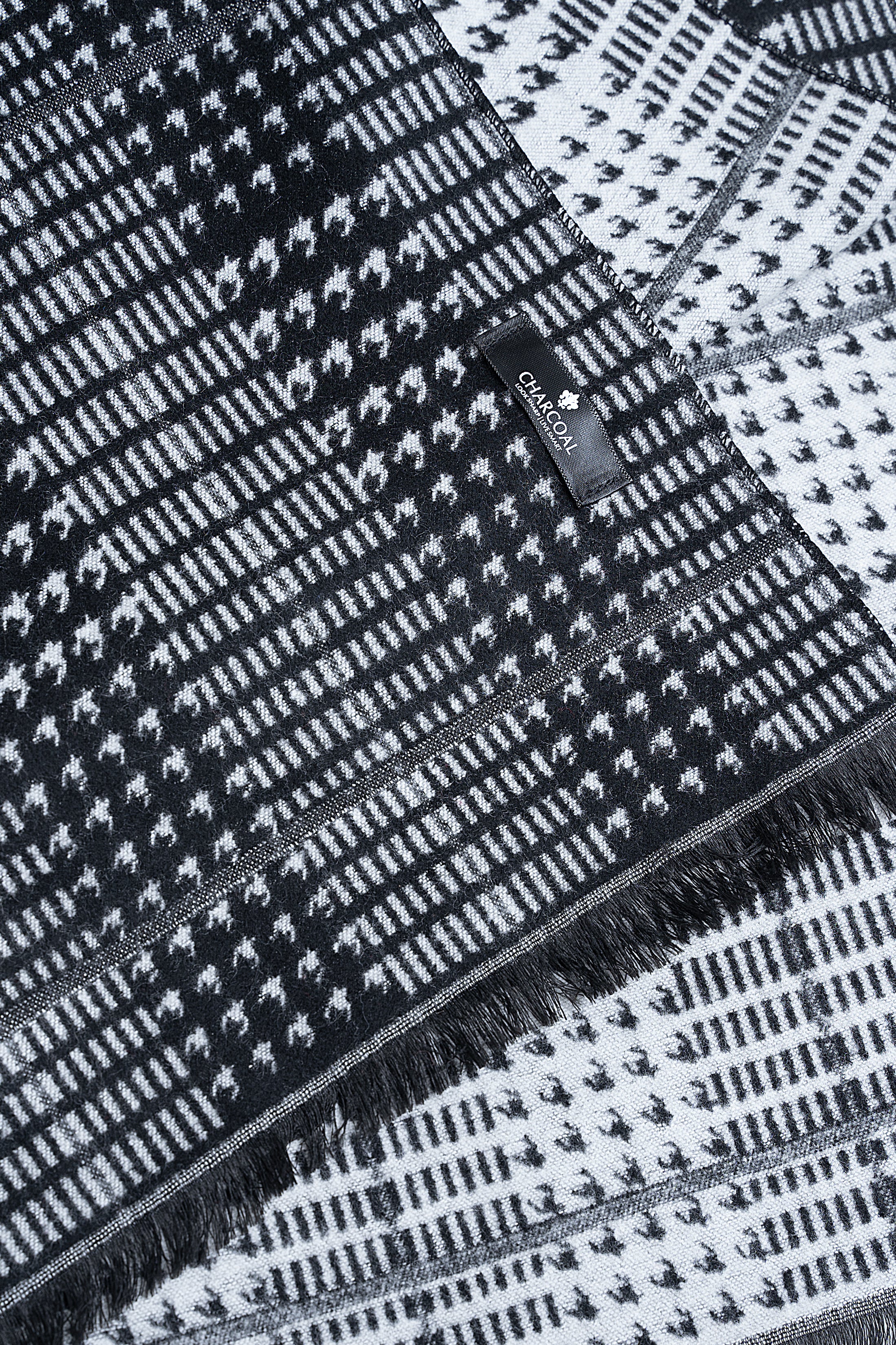Dark patterned scarf close-up with fringed border and woven grid texture.