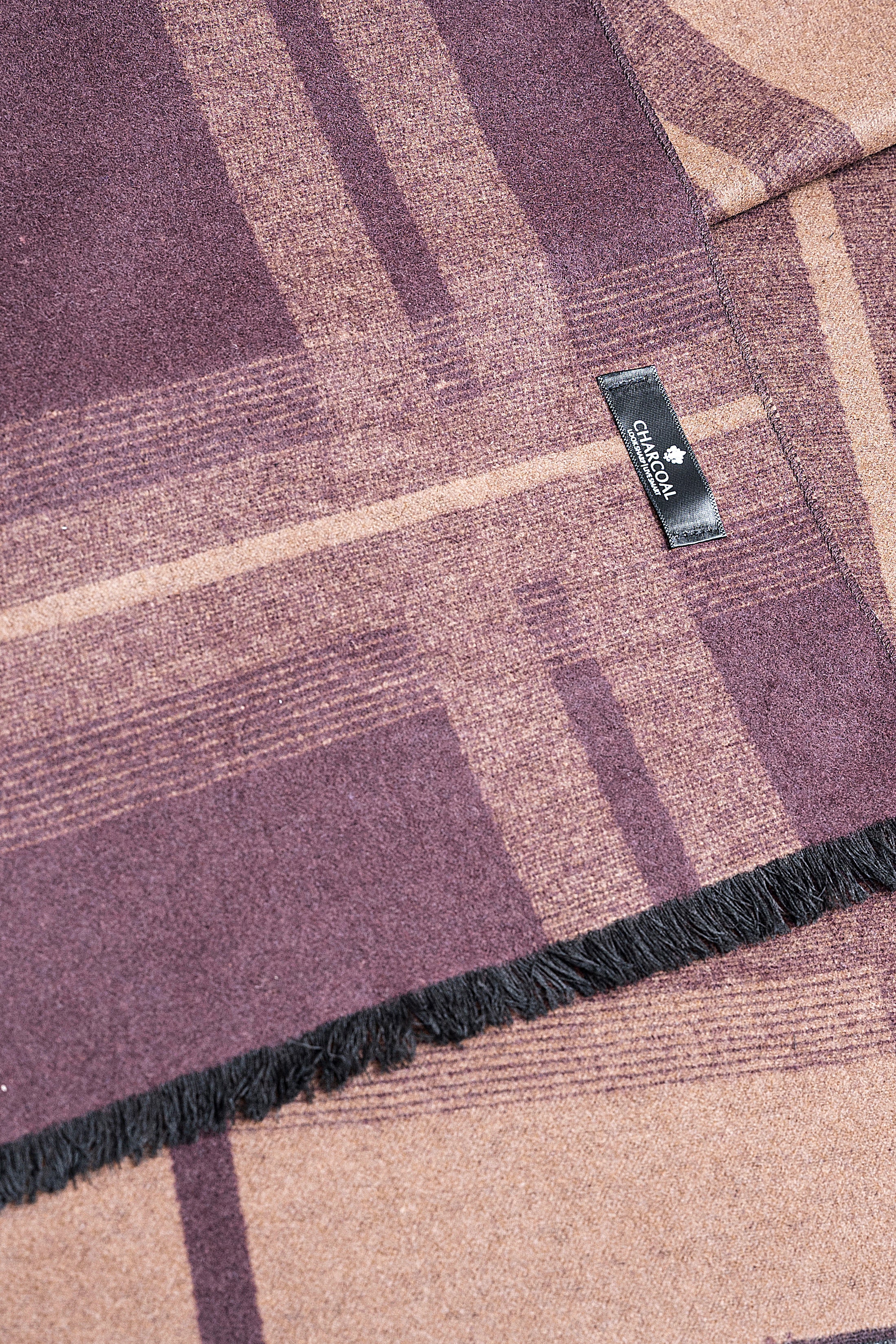 Scarf close-up with mauve-and-tan plaid, black fringe edge and woven label