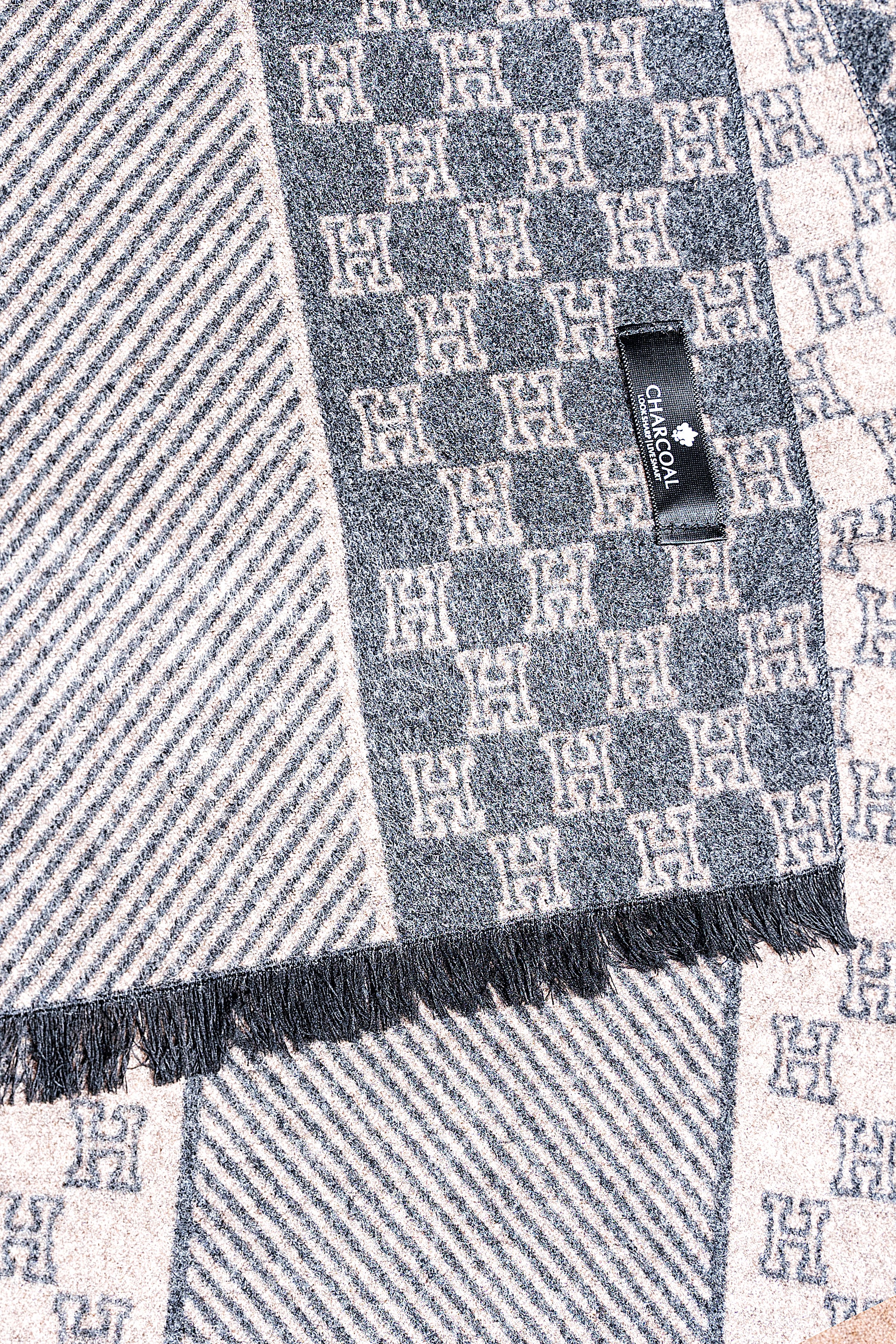 Blue and gray scarf close-up with monogram pattern, black label, and fringed edge