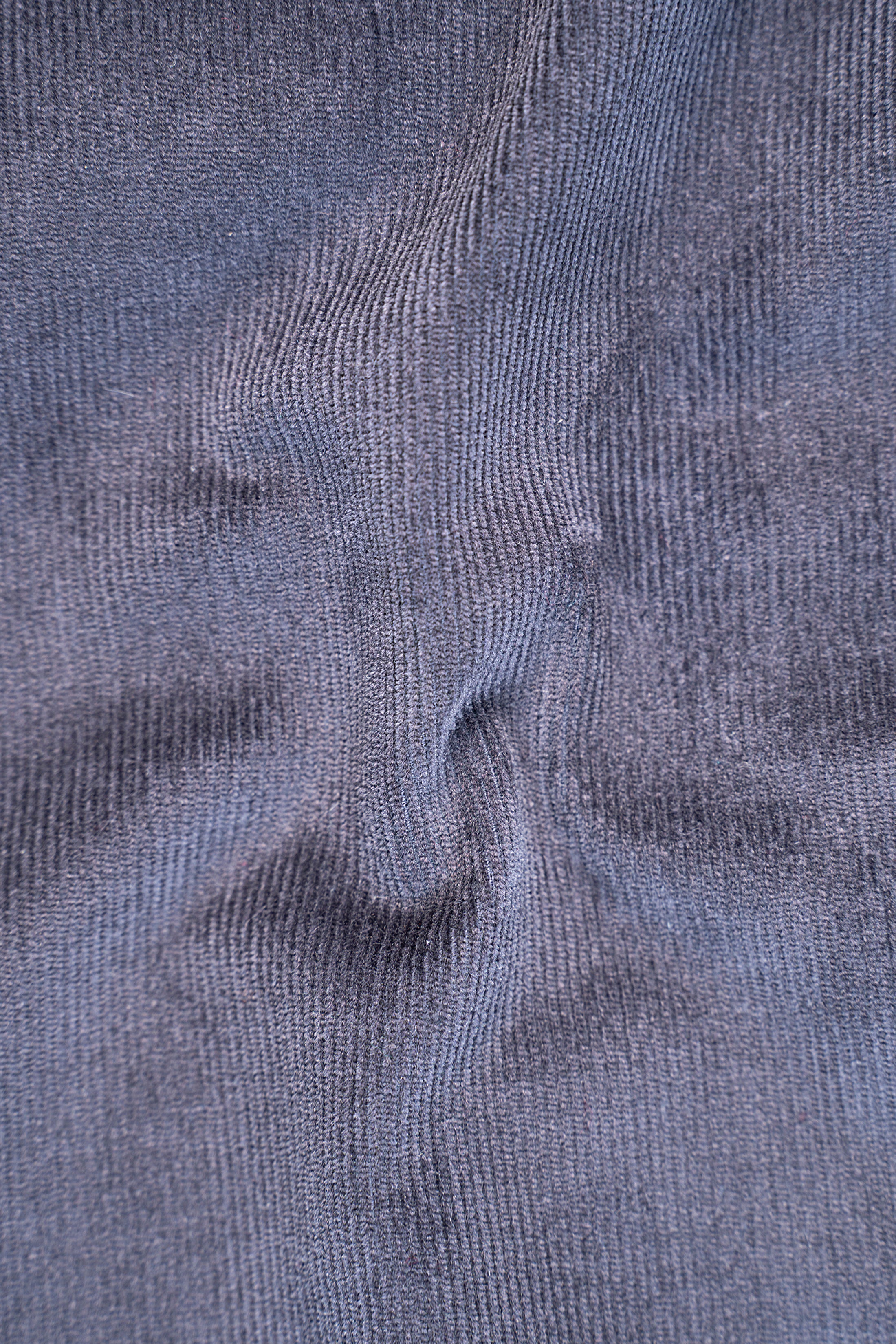Grey corduroy shirt fabric close-up with vertical ribbed texture and seam