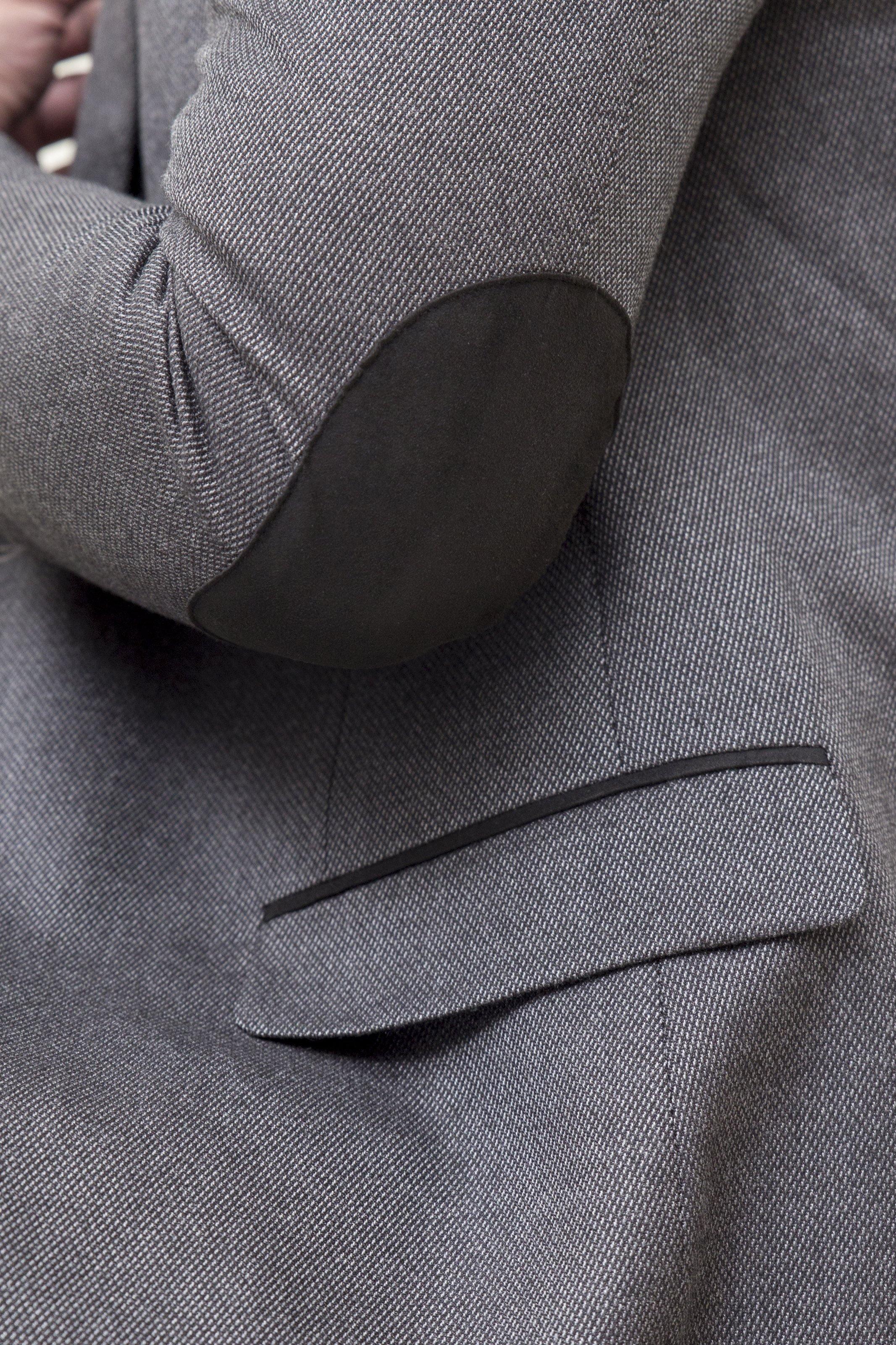 Dark grey coat pocket flap and welt with textured fabric close-up.
