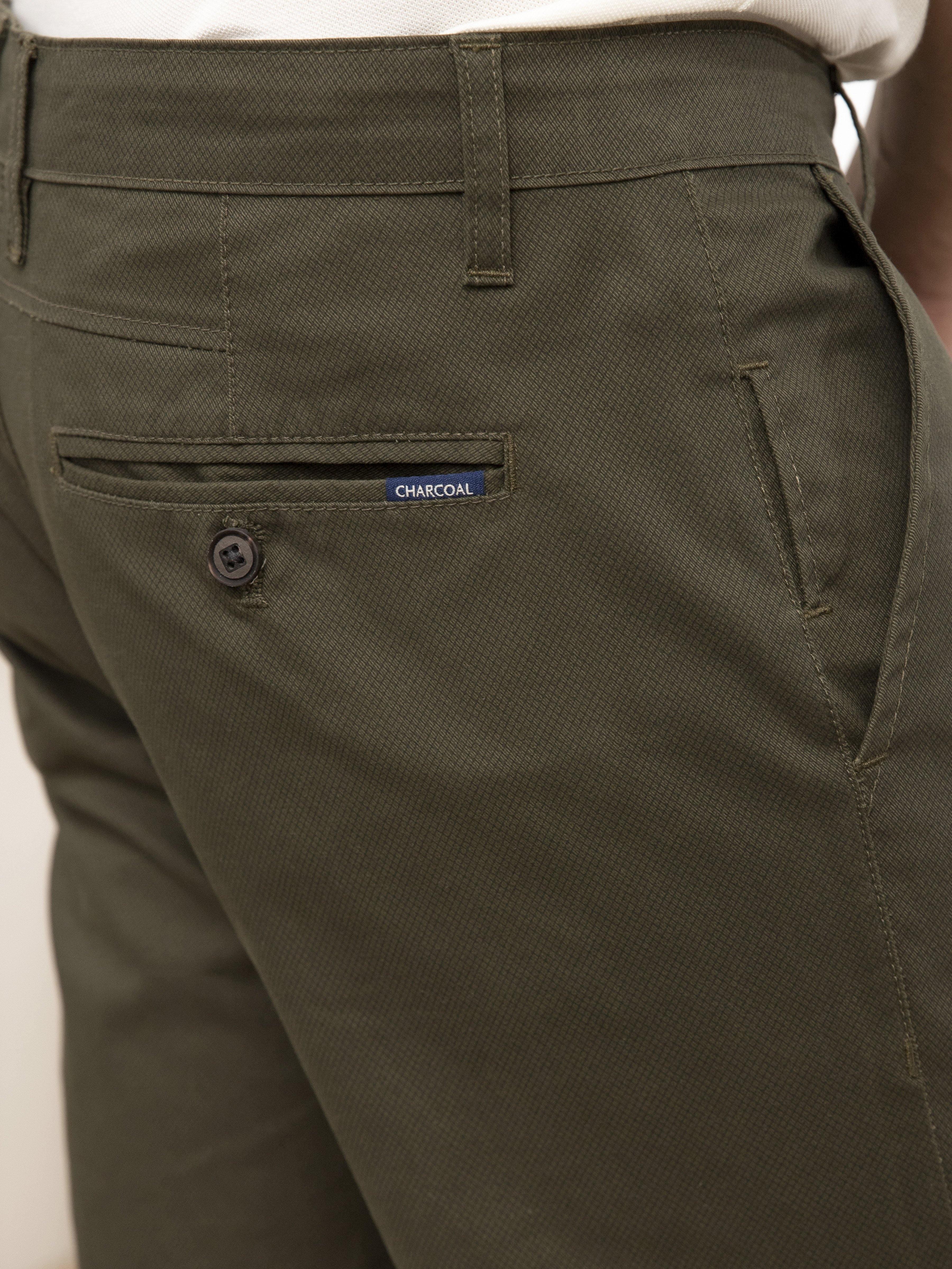 Olive slim-fit pants, front view of pocket and waist button closure