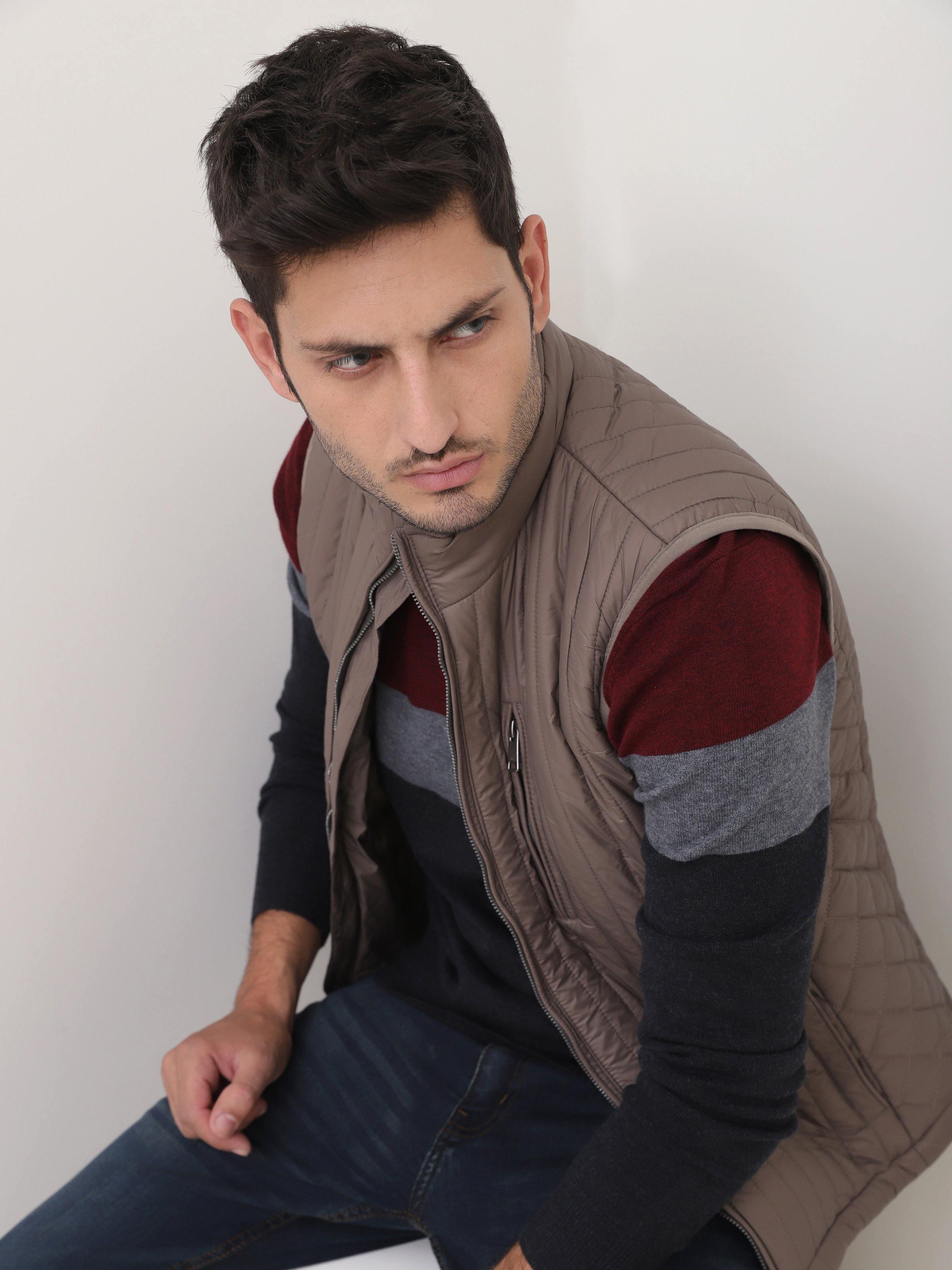 Taupe quilted sleeveless jacket with front zipper and stand collar, model leaning forward