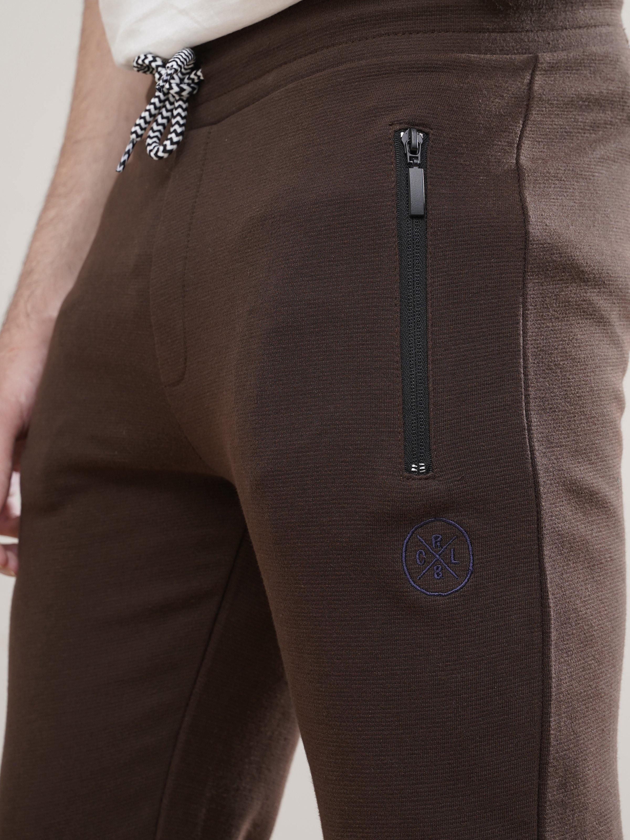 Dark brown jogger trousers close-up of front zip pocket and logo patch