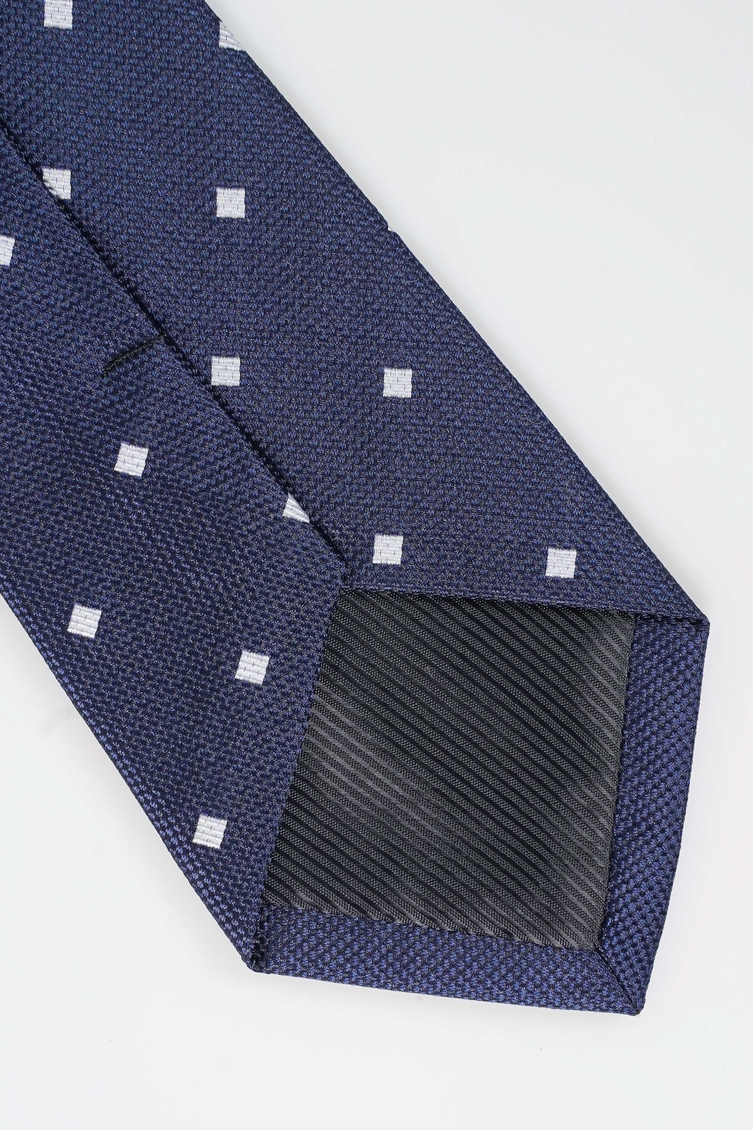Navy tie with white square dots and textured underside on the folded tip