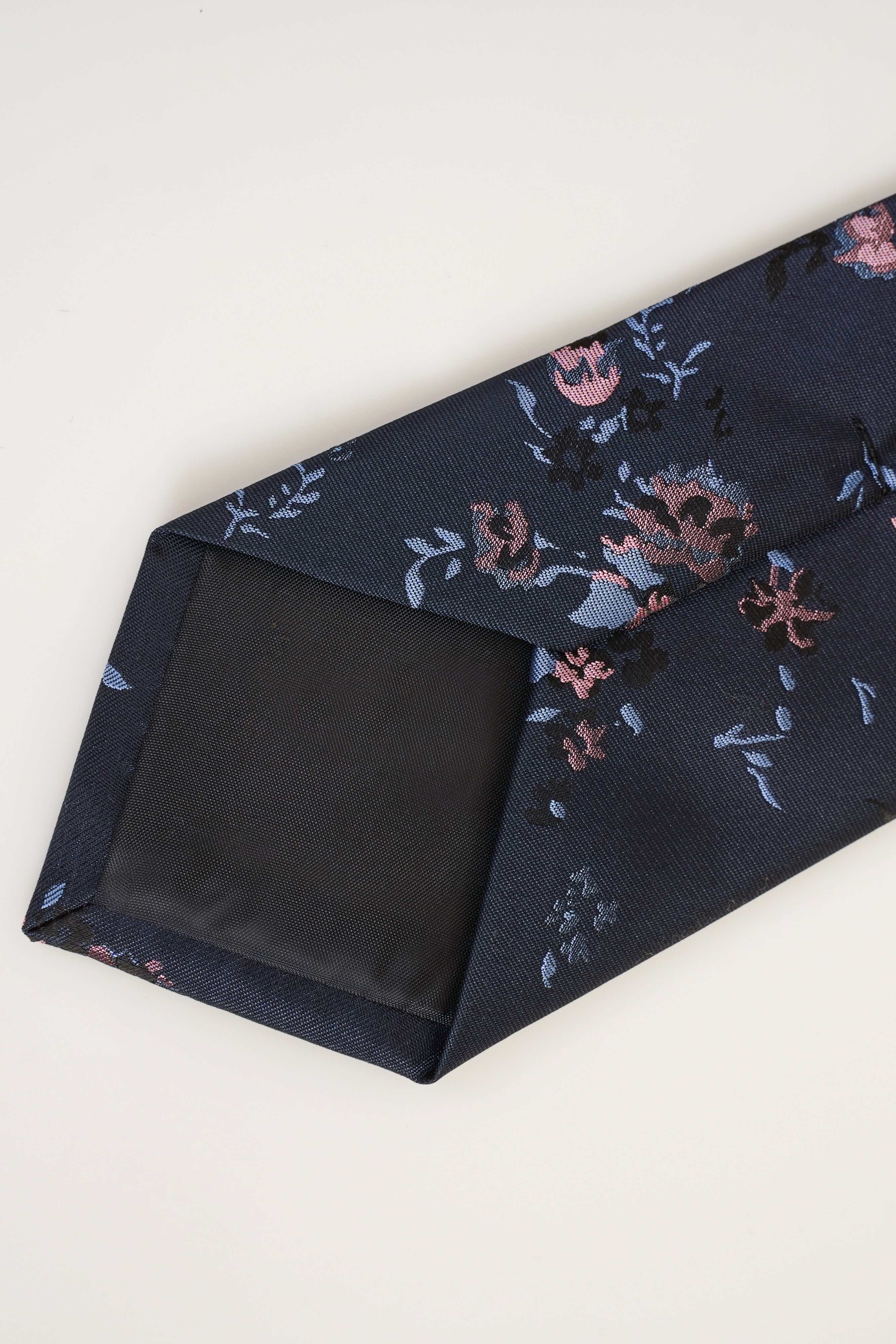 Poly silk tie folded, dark blue with pink and blue floral pattern.
