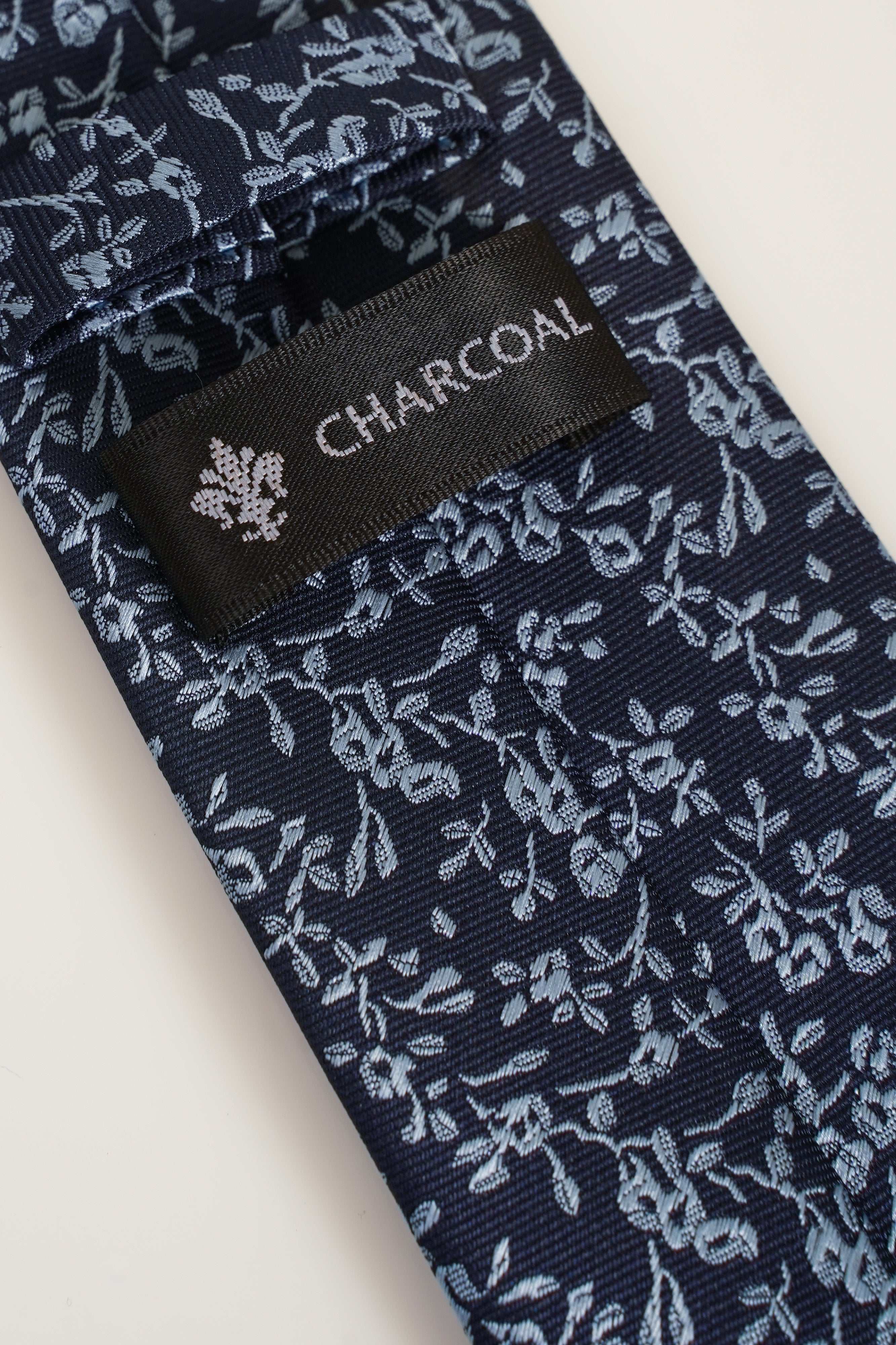 Poly silk tie detail with CHARCOAL label and white floral print on dark navy